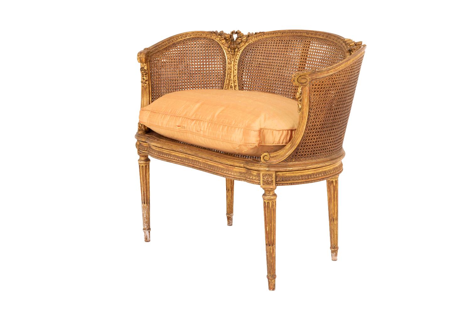 Small Louis XVI style cane sofa in giltwood standing on four tapered fluted and chandelles legs topped by joints adorned with rosettes. Scalloped apron in profile, decorated with a water leaves frieze and a beads frieze. Arm supports on the leg line
