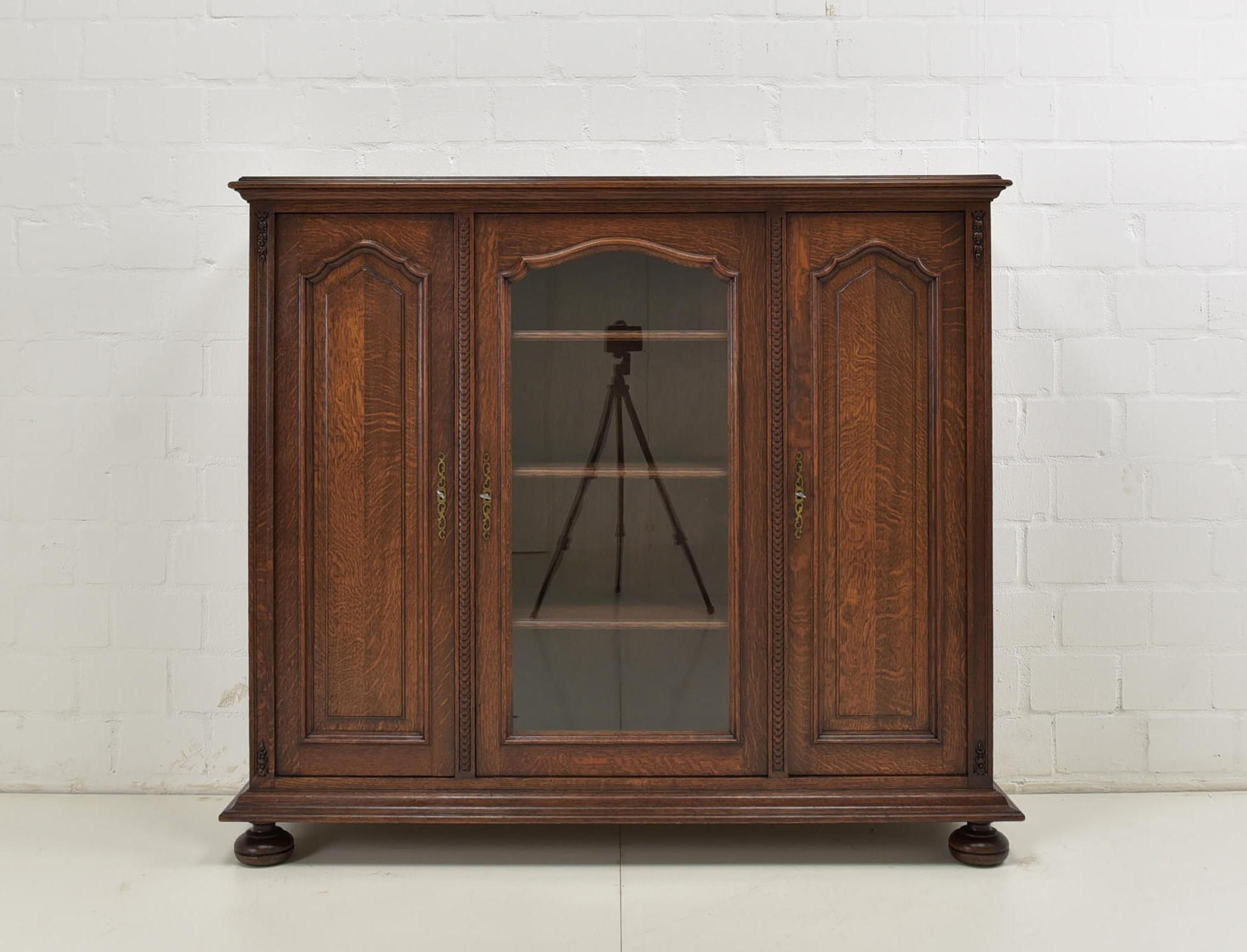 Low display cabinet restored solid oak around 1930 small

Features:
Three-door model with 9 shelves
Height-adjustable shelves
Original glazing
Cassette fillings
Subtle carved decor
Very nice patina
The cabinet cannot be