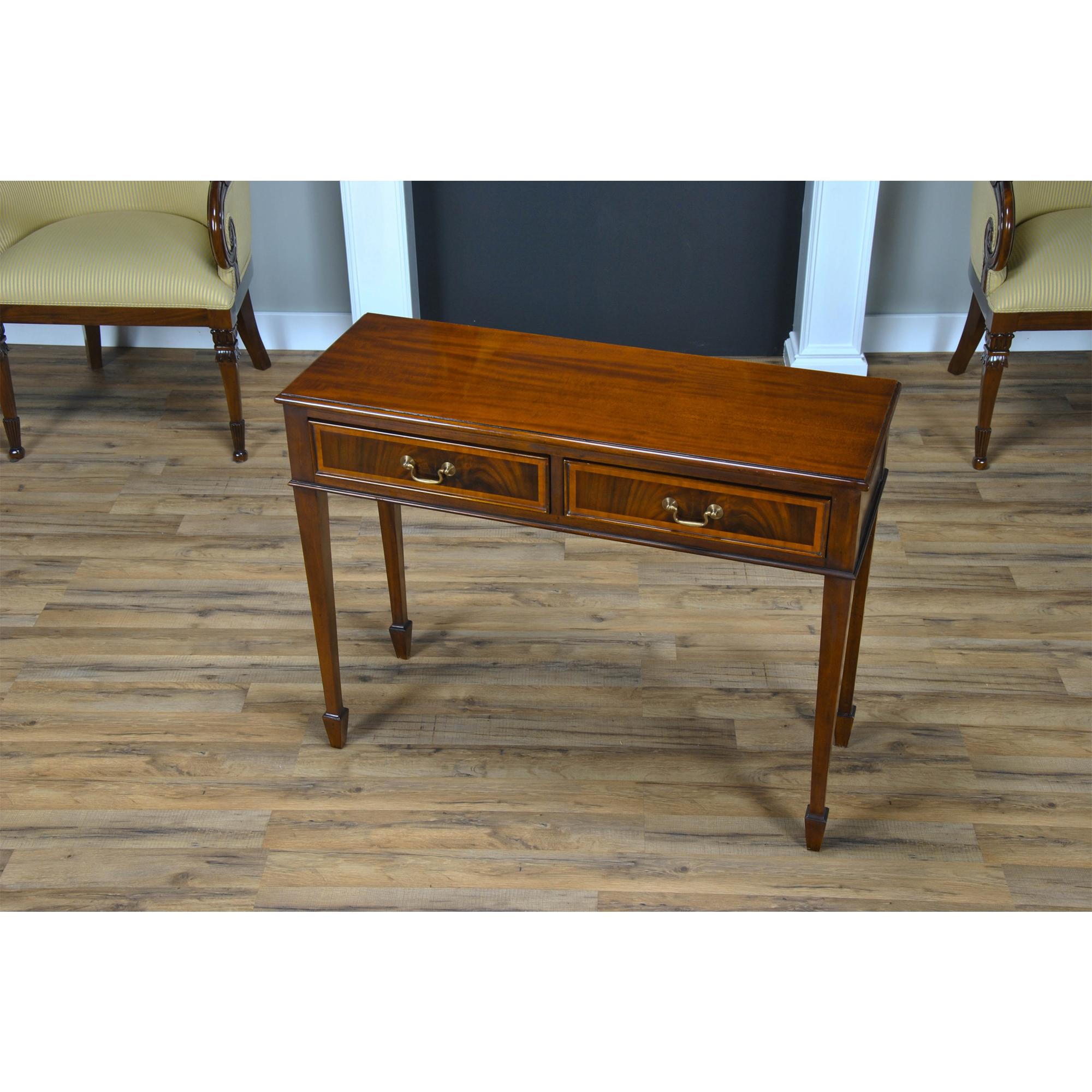 A high quality Small Mahogany Banded Console made of mahogany and satinwood with solid brass drawer pulls. The two dovetailed drawers denote high quality construction and the elegant tapered legs end in a popular spade foot design. A popular piece