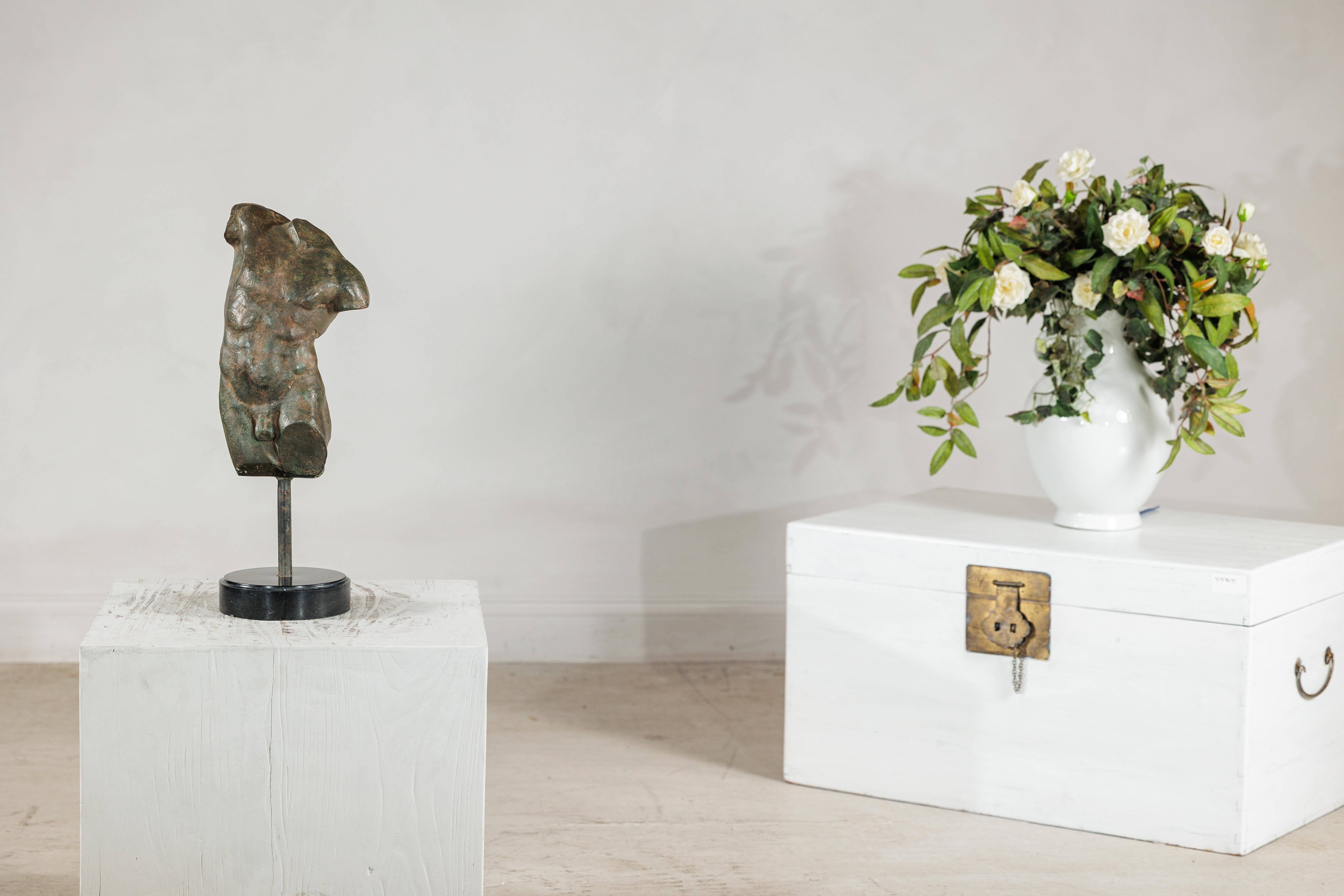 Questo piccolo torso maschile in bronzo è modellato secondo la tradizione classica, presentando una figura frammentata con una muscolatura ben definita e una presenza scultorea che evoca i reperti archeologici. Fusa in bronzo e montata su una base