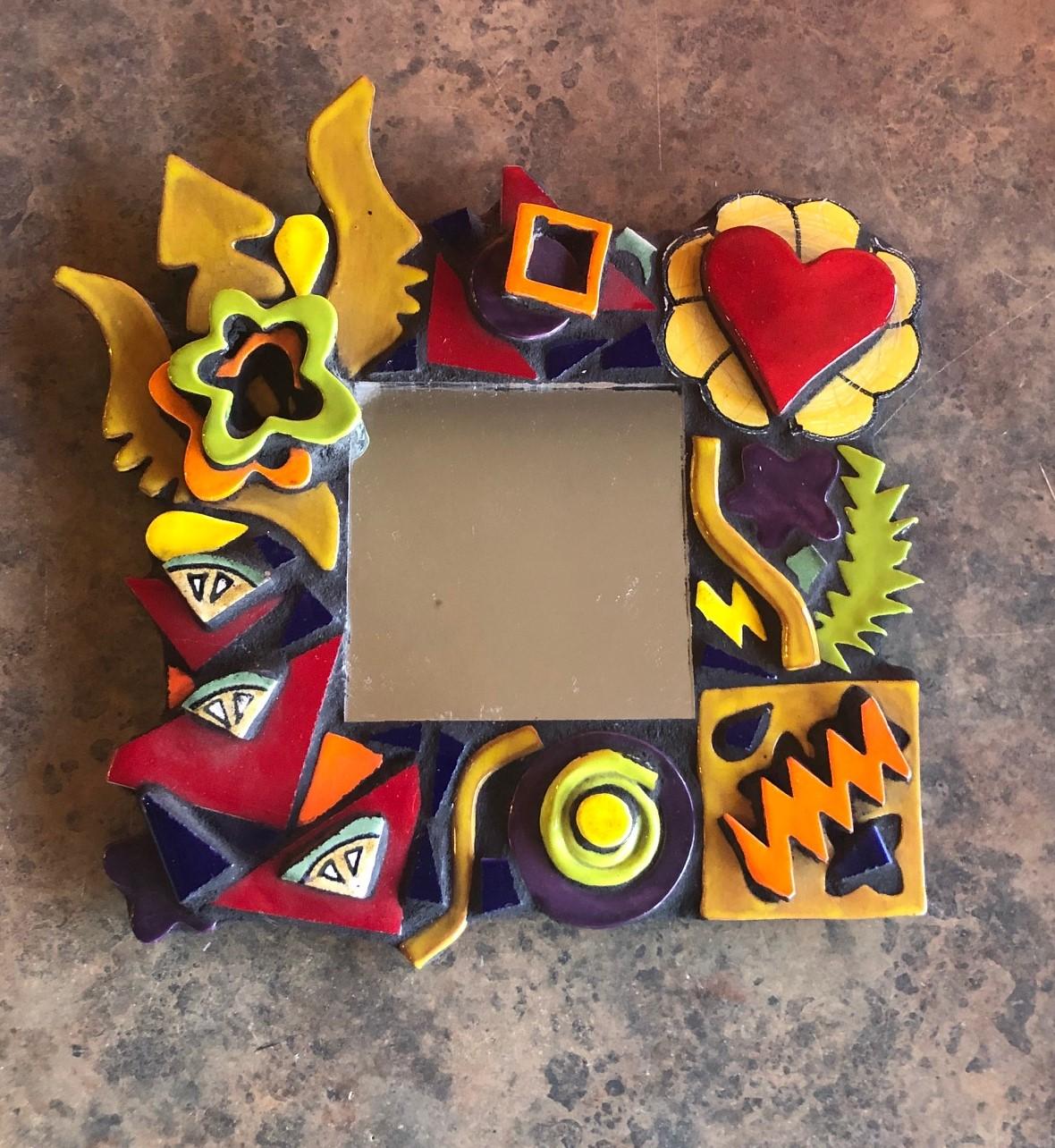 Very cool Memphis style small wall mirror signed Hill Brin, circa 1990s. There is a lot of intricate pottery detail and image overlap on the frame of the handmade mirror.