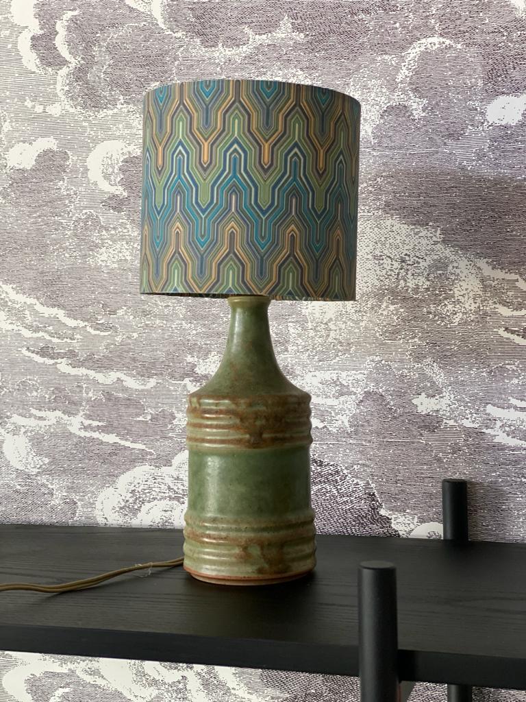 Small ceramic table lamp by Knabstrup from the 1950s from Denmark. The foot of the table lamp is glazed in a beautiful grey-green and reminds by its design of a bottle. The cheerfully patterned fabric lampshade gives the small lamp that certain