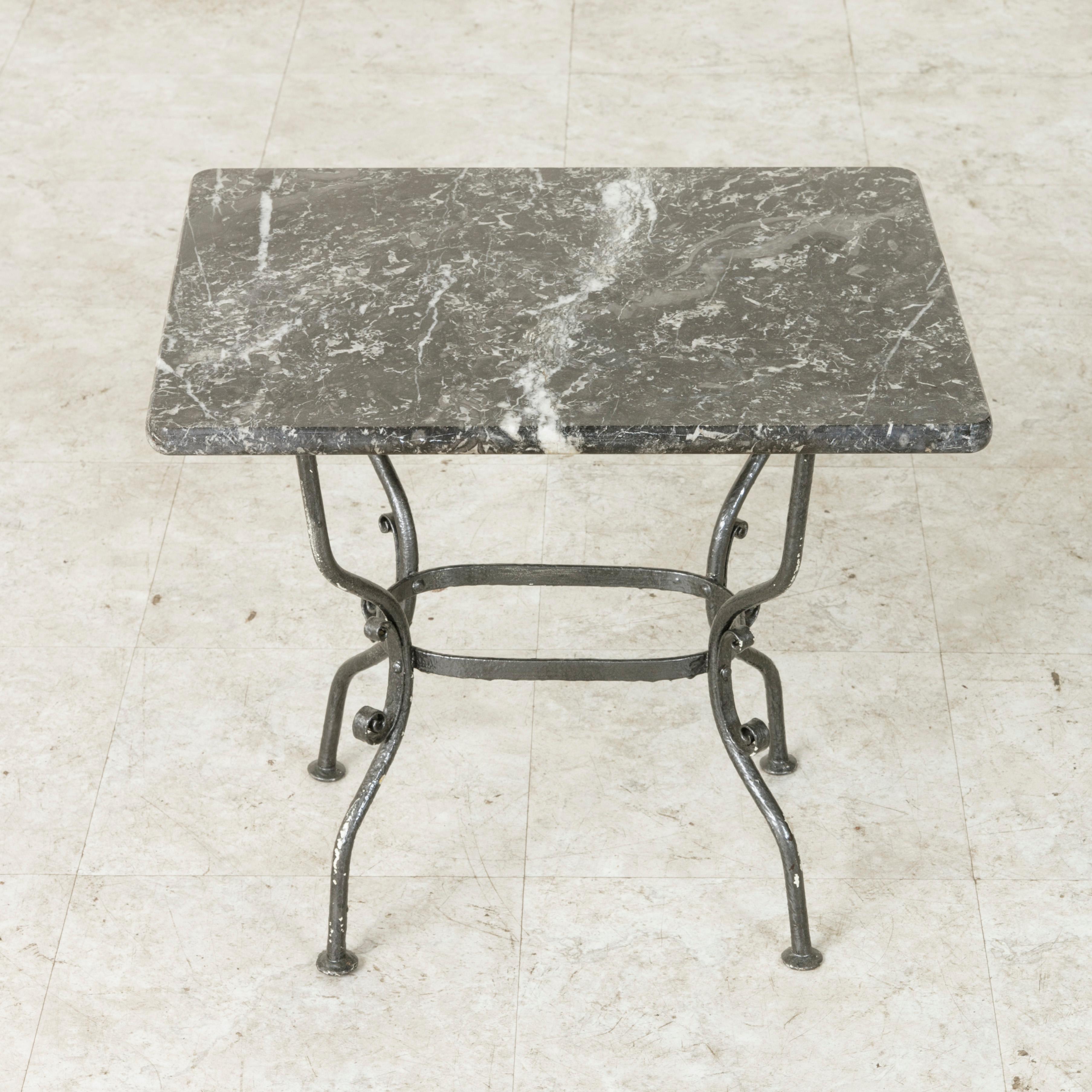 This mid-20th century French side table or end table features a Saint Anne marble top that rests on a hand-forged iron base. The base has four curved legs that are joined by a ring stretcher in the centre and is detailed with scrolling. Its small