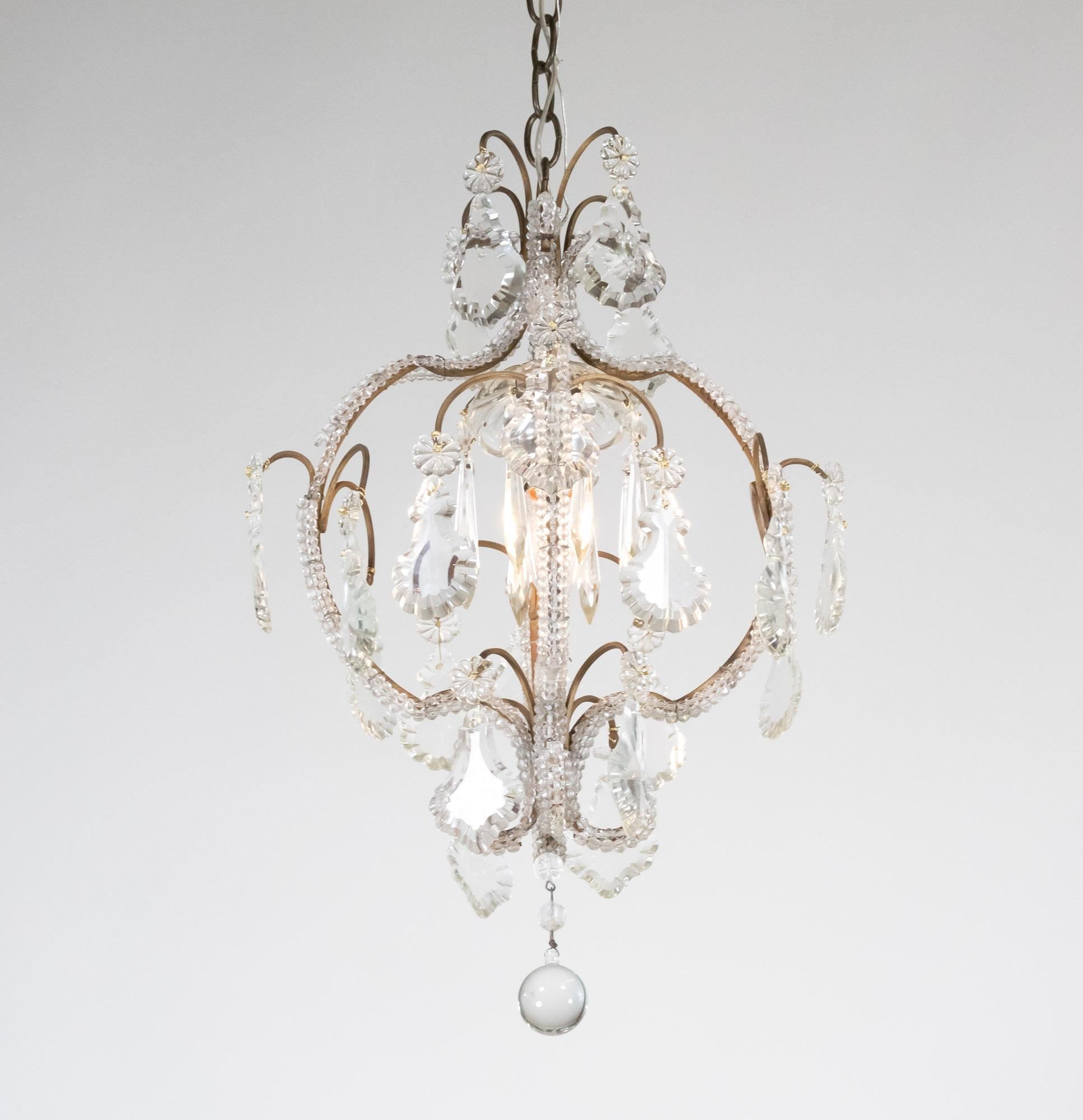 Questo piccolo lampadario italiano della metà del secolo scorso, realizzato in stile rococò, presenta un'armatura in ottone a forma di gabbia di uccello con una sola luce. La struttura in ottone è impreziosita da perline di cristallo sfaccettato,