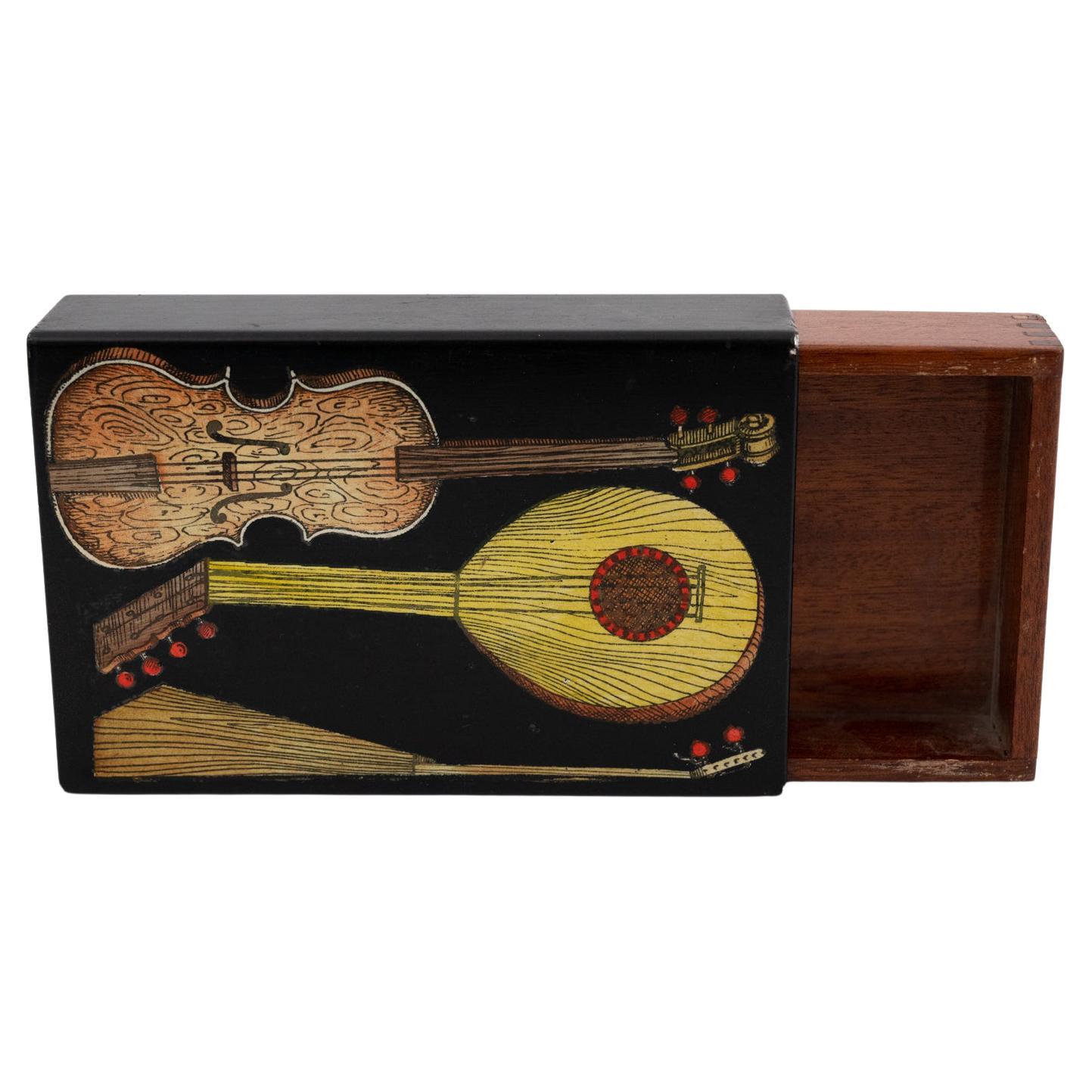 A small Piero Fornasetti box decorated with guitars and zithers
Metal, lithographically printed and hand coloured. 
Mahogany interior, Fornasetti label to the base.
Italy, circa 1960. 

Piero Fornasetti was one of the most prolific creators of
