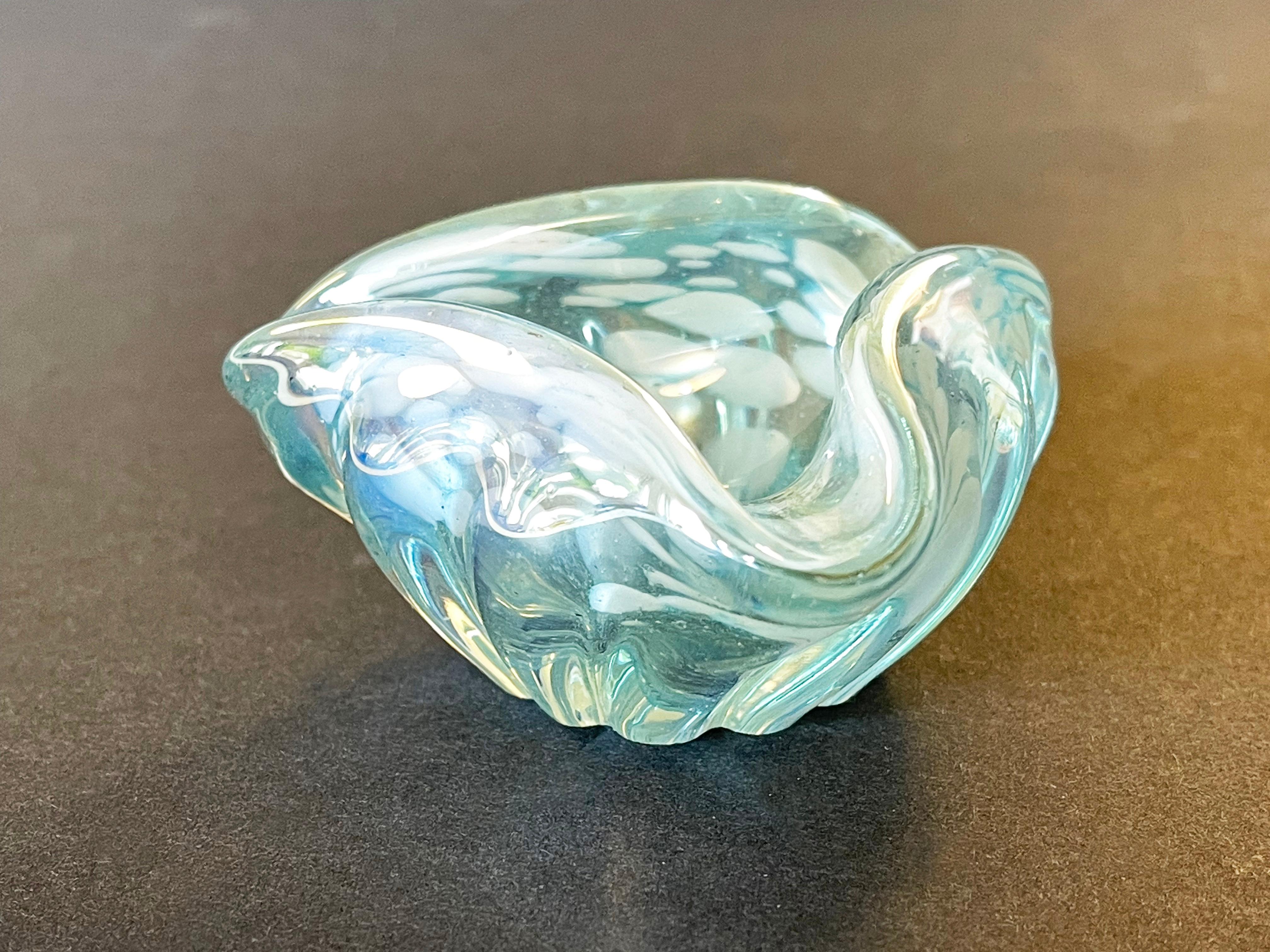 Very sweet little Italian triangle astray from Murano: here in a light blue with white swirly spots and tiny air bubbles and dark spots.
The glass surface reflects in the colours of mother of pearl.
A typical 1960s original from Italy.
