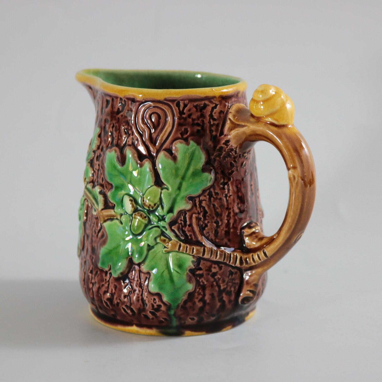 Minton Majolica jug/pitcher which features oak leaves and acorns to the sides and a snail to the handle. Colouration: brown, green, yellow, are predominant. The piece bears maker's marks for the Minton pottery. Bears a pattern number, '553'. Marks