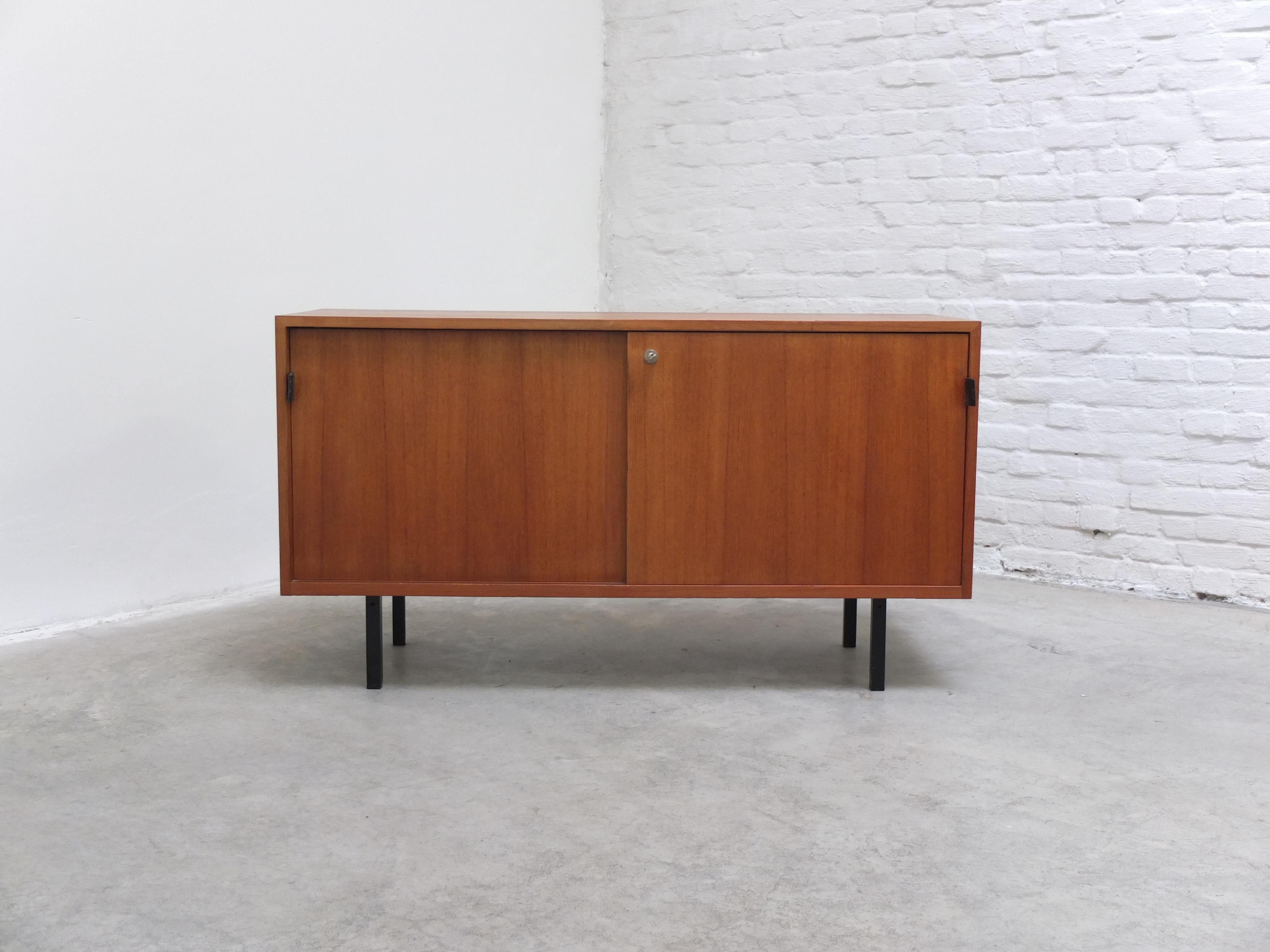 Small modernist sideboard designed by Florence Knoll Basset during the 1950s. This model is made of teak wood with leather handles and black metal square legs. Florence Knoll is known for a wide range of high-end minimalistic sideboards and these