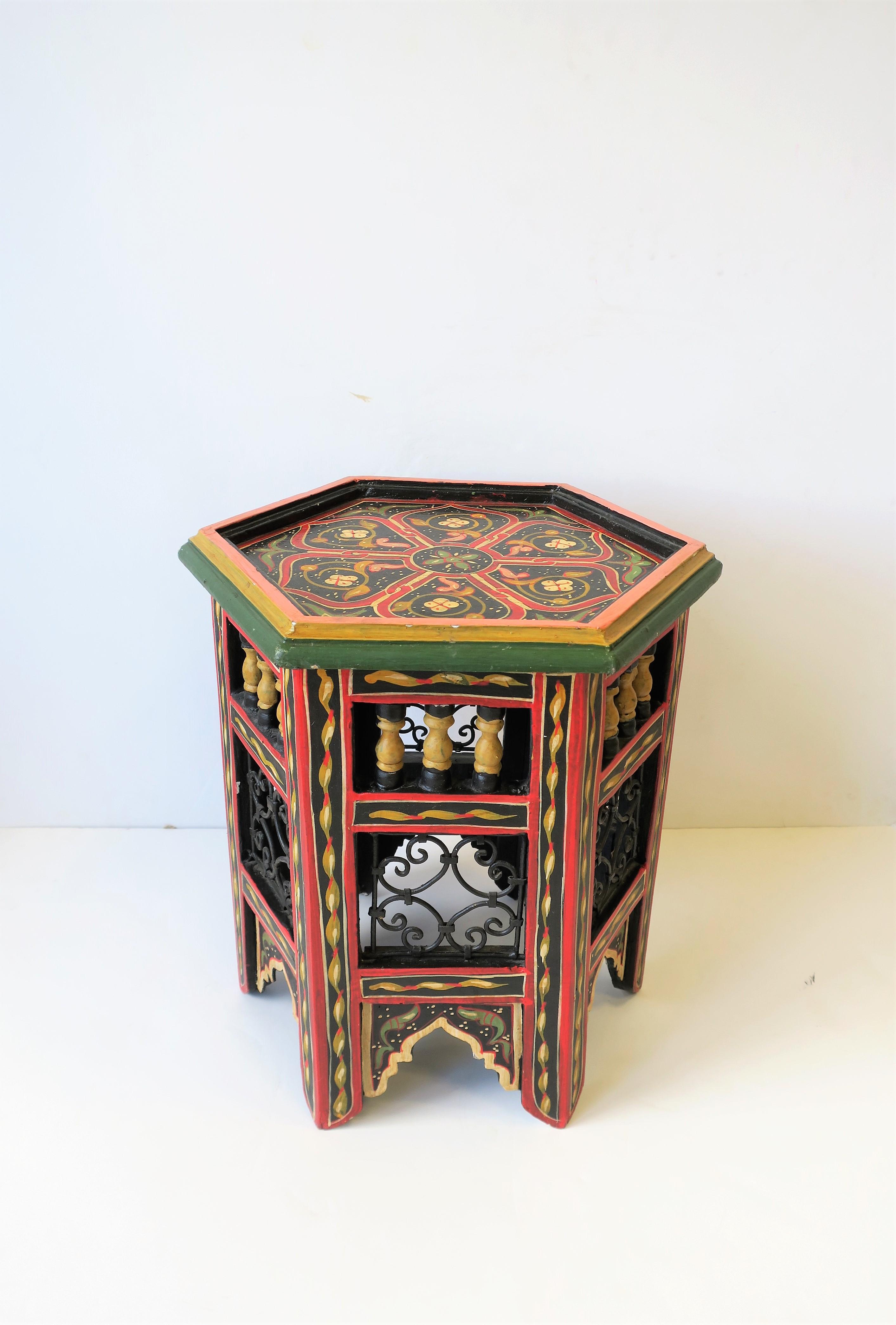 A small colorful Moorish or Moroccan tabouret side or drinks table with a hexagon top, decorative design, and black metal on sides, circa mid-20th century. The carnation pink, dark yellow, and green grass colors around edge of hexagon top make a