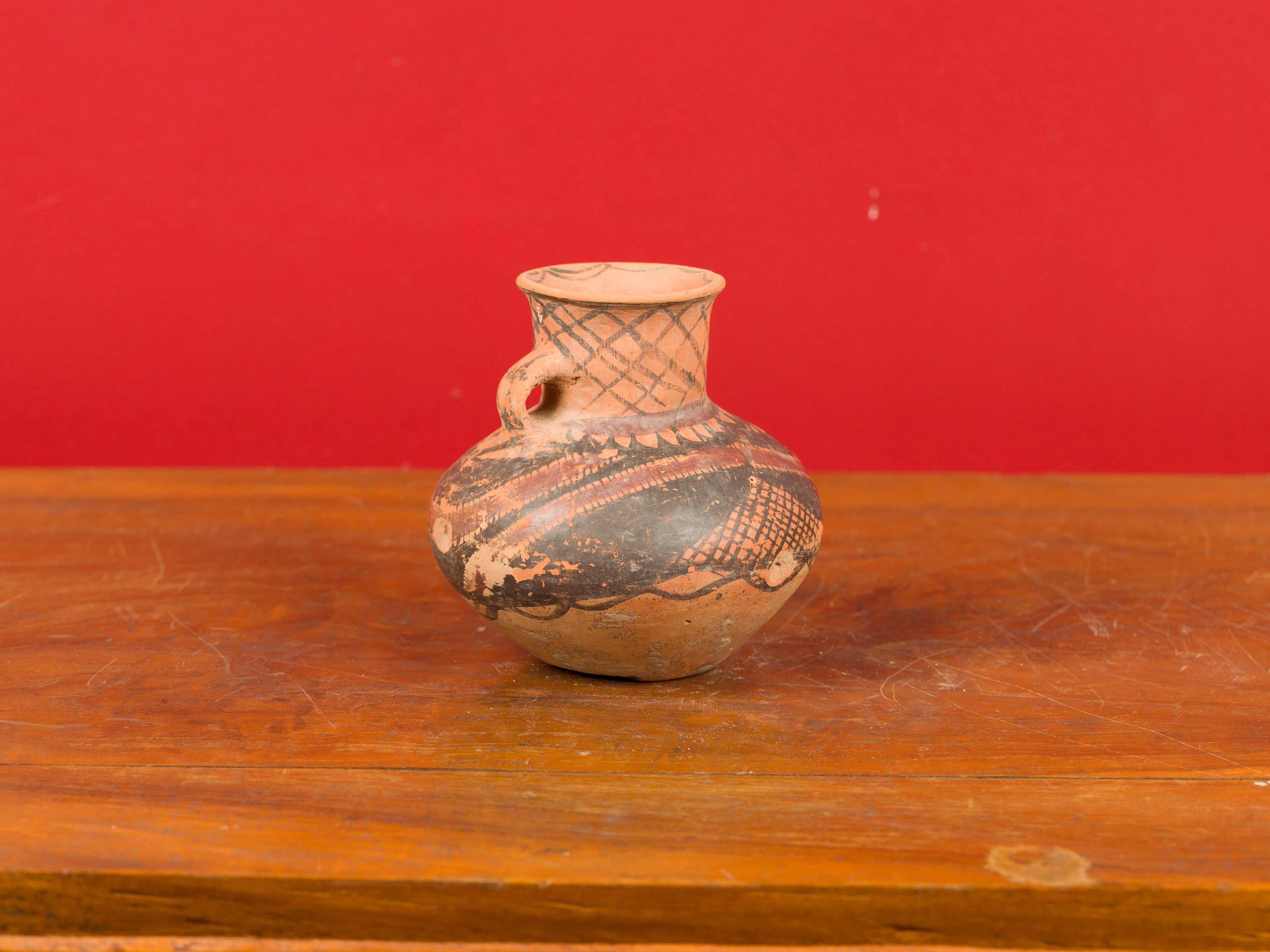 A Chinese Neolithic terracotta pottery from 4000-3000 BC, with single lateral handle and red and black painted geometric decor. Born in China during the Neolithic period, this pitcher attracts our attention with its nice patina, simple lines and