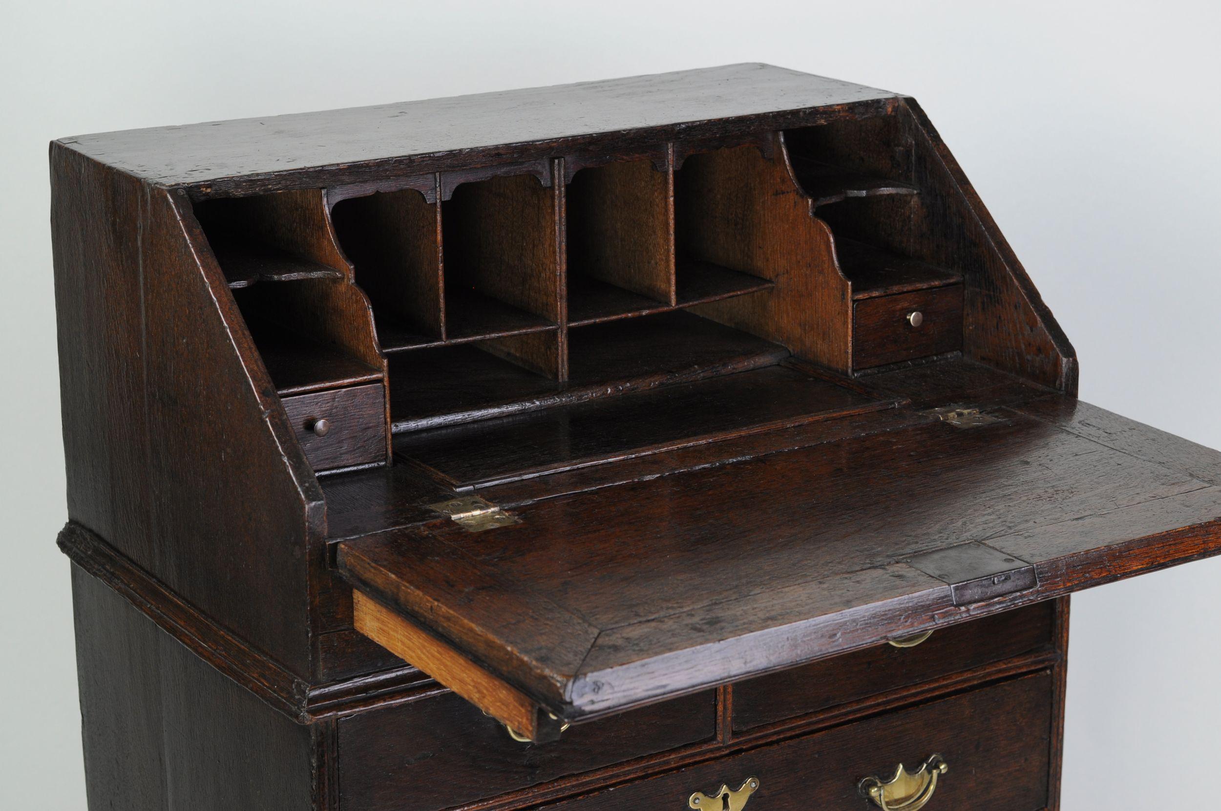 A rare 18th century oak bureau of particularly small and diminutive proportions. the fall with a moulded book-rest, opening to reveal a stepped interior with a well concealed below a false drawer-front, above a waist moulding and arrangement of two