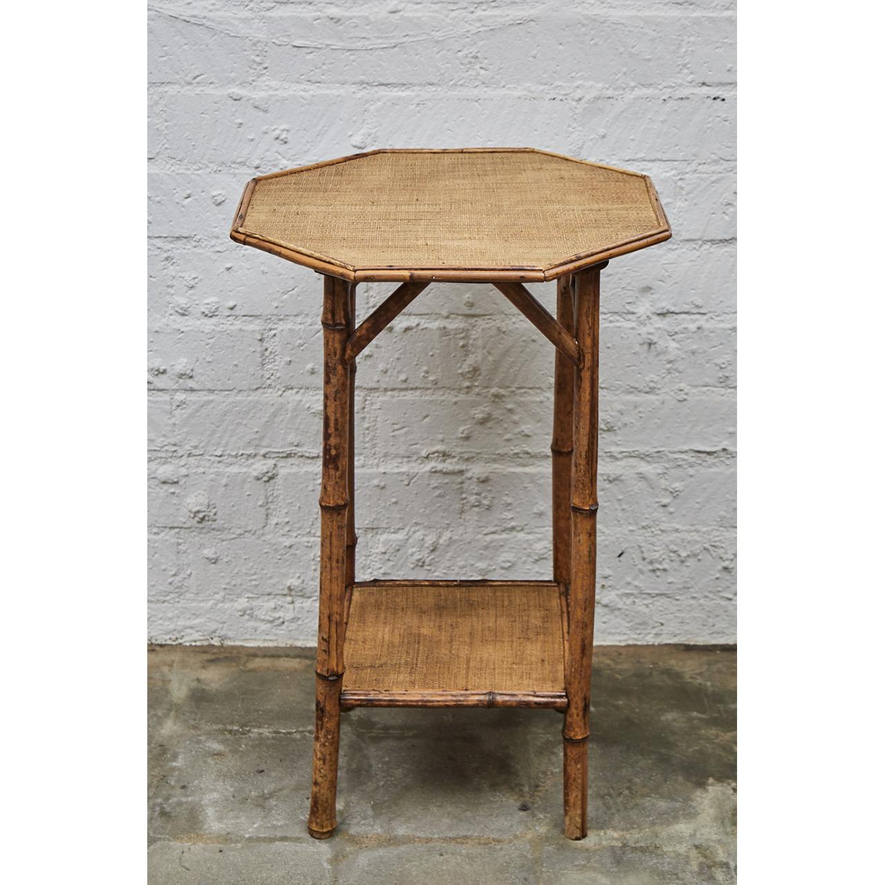 This Victorian side table is made of tiger bamboo with newly re-surfaced waxed raffia matting. The table has an octagonal top and square shelf. The straight legs have diagonal supports and have been reinforced with dowels for increased sturdiness.
 