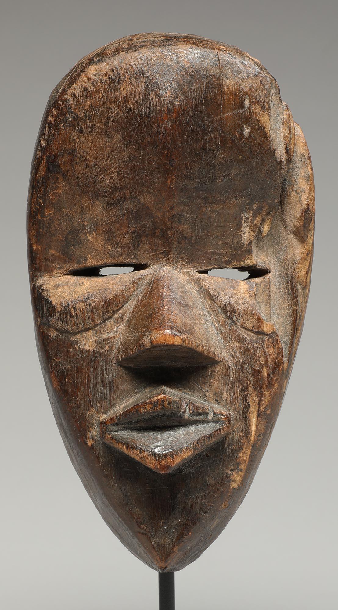 A small old carved wood Dan mask with cubist face. Blessed by time, weather and insects, with erosion to the right side of head. Mask was probably stored or abandoned on the ground where the insects got to it. Old wear and staining on inside from