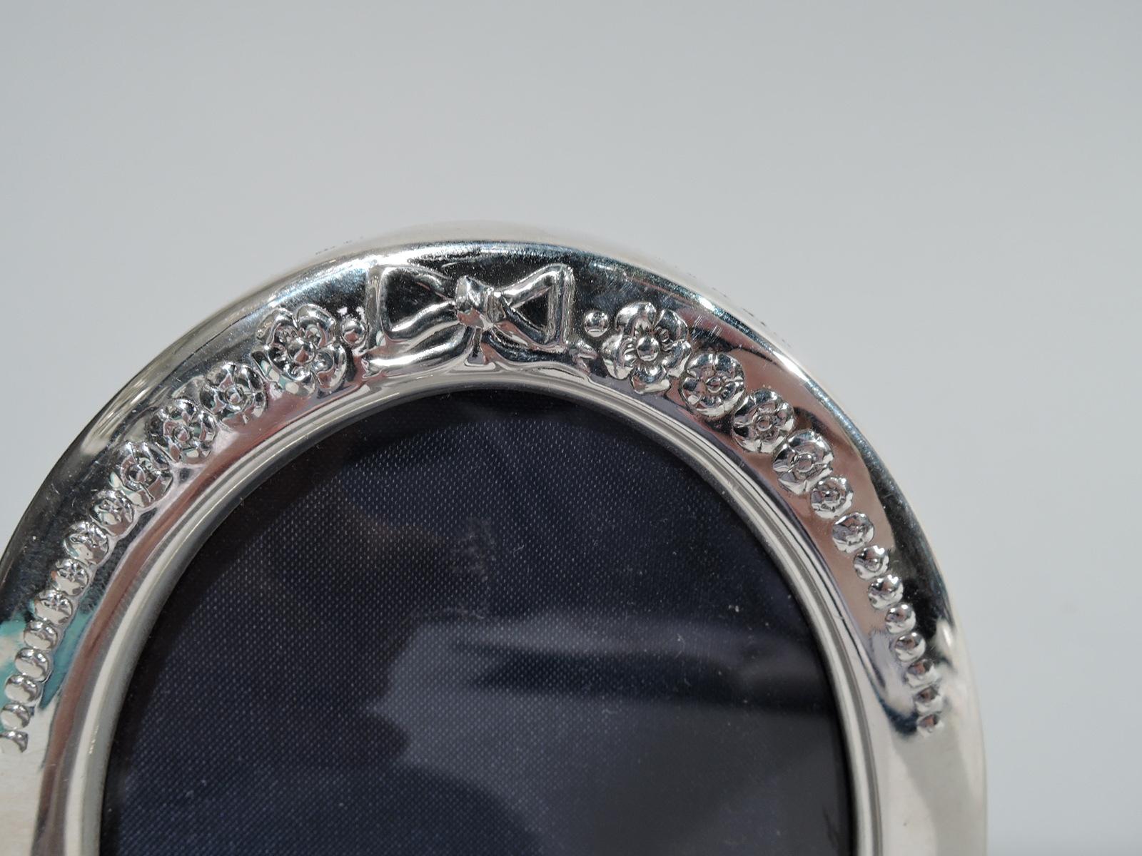 Old fashioned sterling silver picture frame. Made by Carr’s of Sheffield in 1990. Oval window and surround with chased bow and blossoms graduating to beads. With glass, silk lining, and velvet back and hinged support. Hallmarked. 

Dimensions: