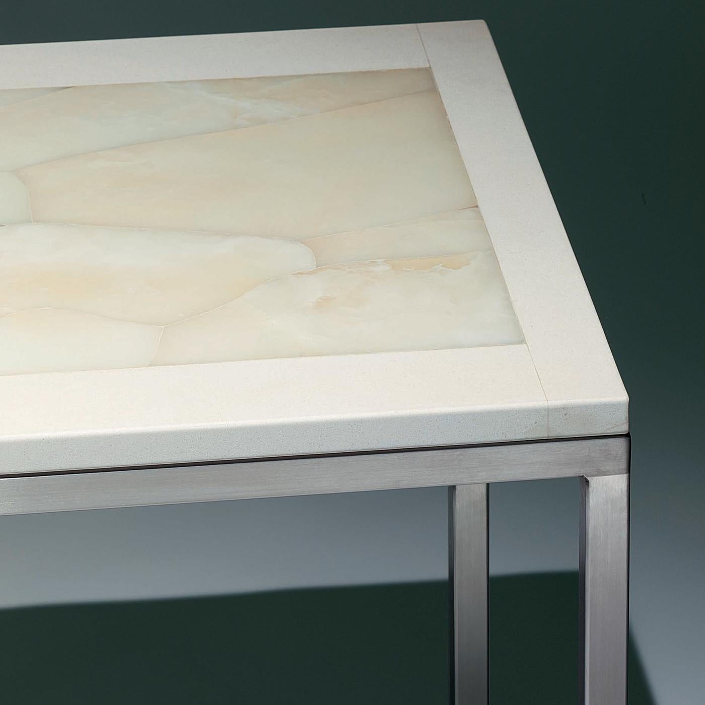 This side table features a hand inlaid white onyx top trimmed in ivory-colored limestone. Its matte, smooth surface provides a serene, calm look. Polished stainless steel legs complete the item with an added touch of sheen. This clean-styled,