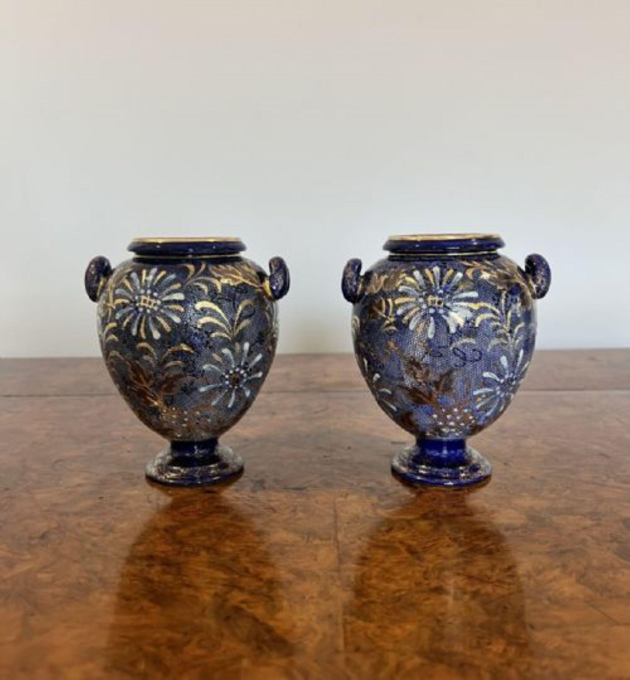 Small pair of  antique Doulton vases having a lovely pair of antique Doulton vases decorated with golden and white flowers on a blue background with a shaped body standing on circular bases. 