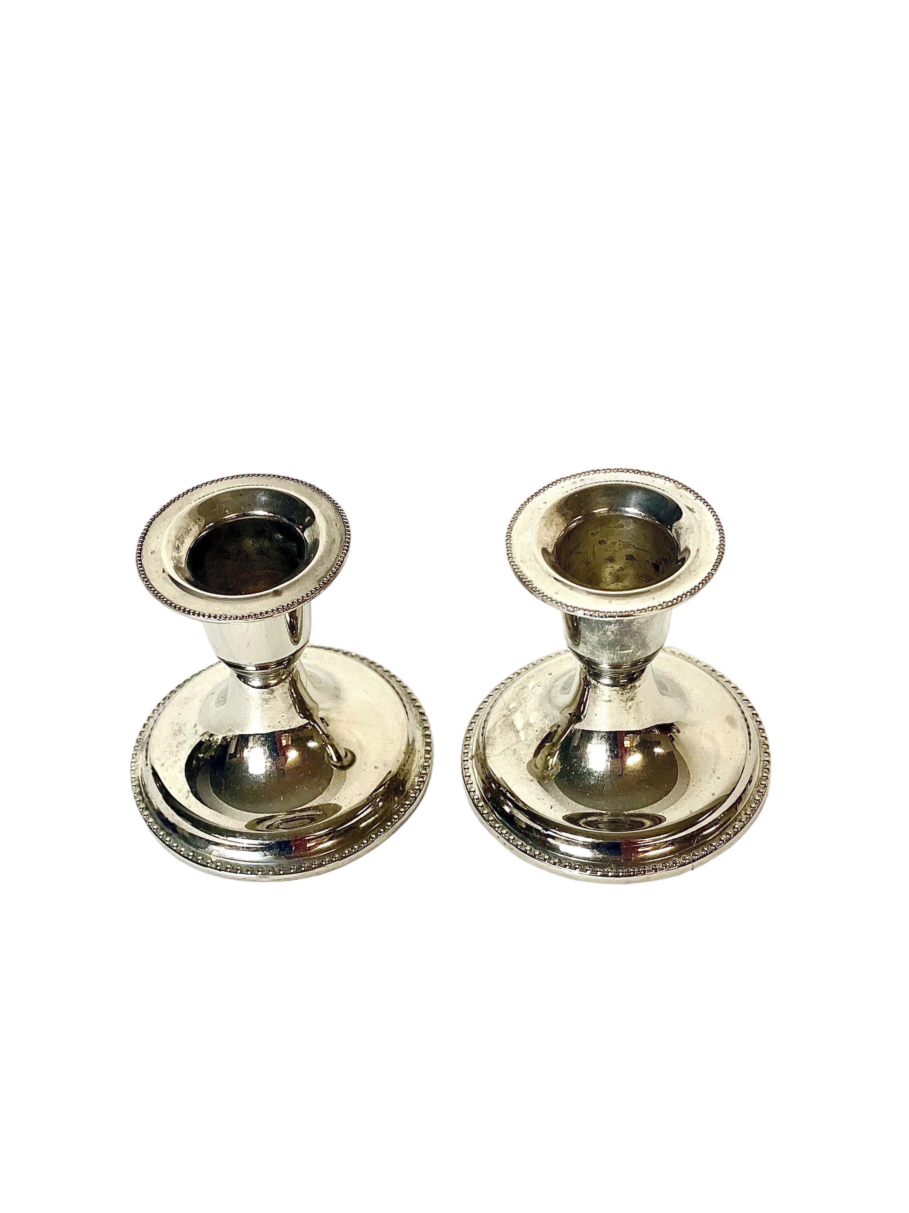 A pair of small, antique Louis XVI style silver-plated candlesticks, with a beaded pearl pattern around the upper rim and the gently flared pedestal base. This matching pair would ideally suit a smart dining table or a mantelpiece.