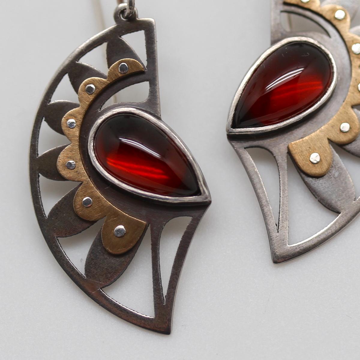 The classic Metaalia Jewelry earring design inspired by South Asian textiles and Native American pottery glaze designs. A blend of ornate and graphic. Pierced and hand-riveted oxidized sterling and brass. Sterling bezel-set pear-shaped garnets.