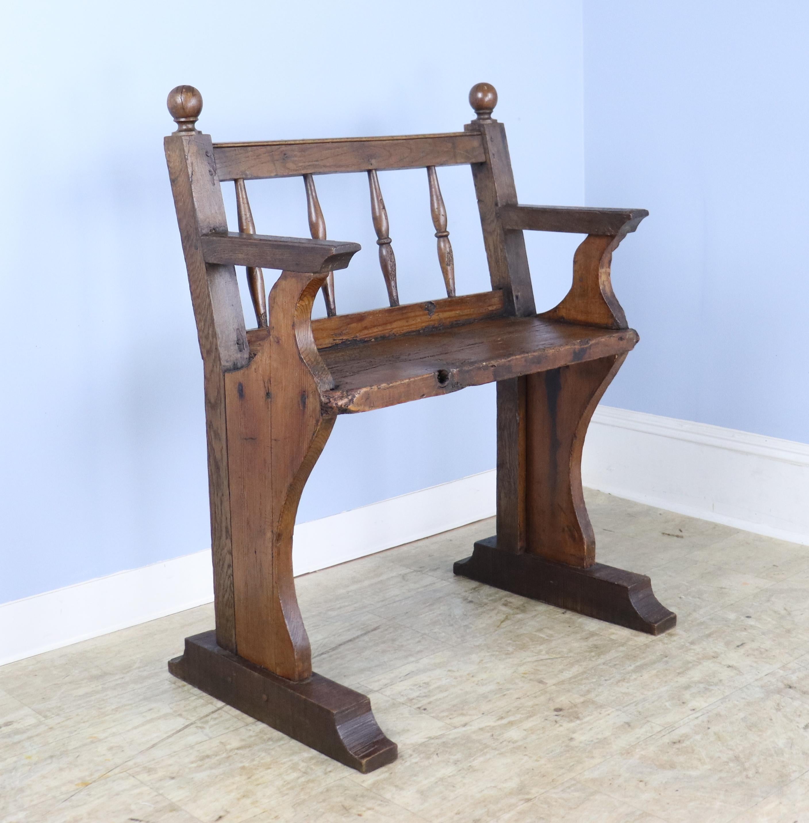 A small distressed oak and pine bench with probable industrial origins, such as a train station.  Charming details include round finials and well articulated spindles on the back.  There is a large natural knothole on the seat, shown in thumbnails.
