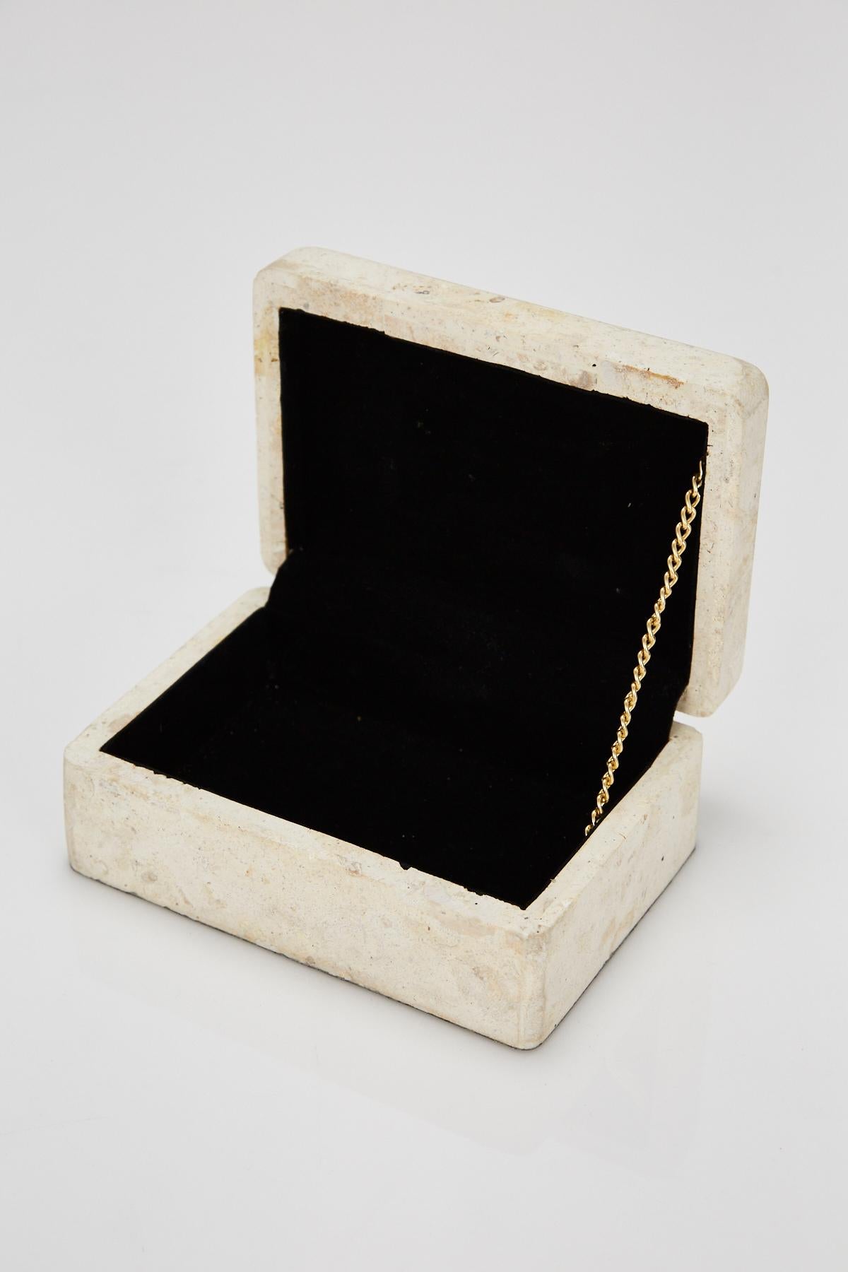 Small lidded box in matte white tessellated Mactan stone exterior and black felt-lined interior. Brass chain connects top and bottom. Underside lined in black felt. Simple rectangular form with lightly curved edges.