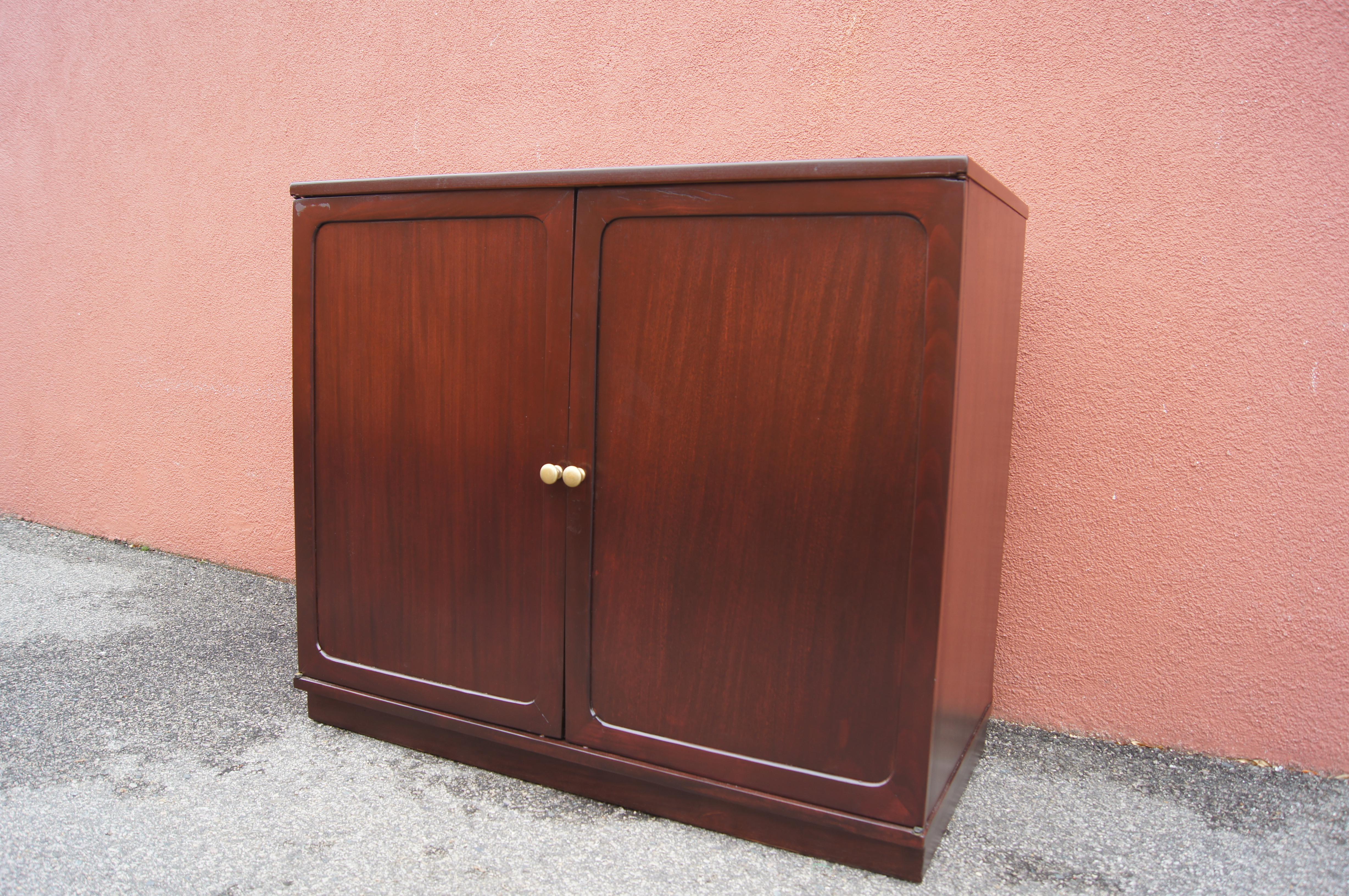 From the Precedent line of North Carolina–based Drexel furniture, this small cabinet features two deep tray-style shelves that slide out for easy access. The exterior of the bleached mahogany cabinet has been stained a dark cherry; the doors open