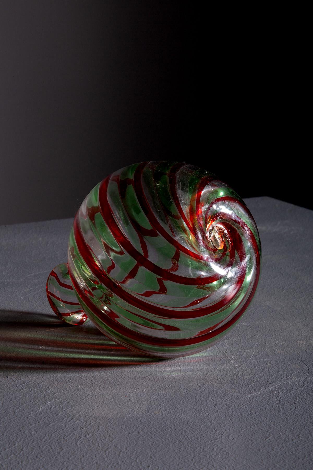 This enchanting Murano glass vase, crafted in the 1960s, is a true gem of Venetian glassmaking art. Its captivating and sinuous design, adorned with delicate filigree lines, immediately draws attention with vibrant tones of red and green swirling
