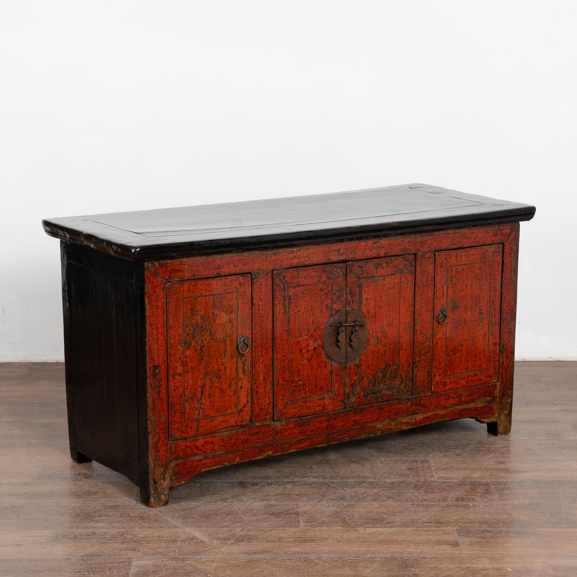 The red lacquered polished finish with contrasting black top on this small Chinese sideboard provides a modern look allowing it to serve well in a contemporary setting. 
The original red painted finish was worn down throughout to reveal the natural