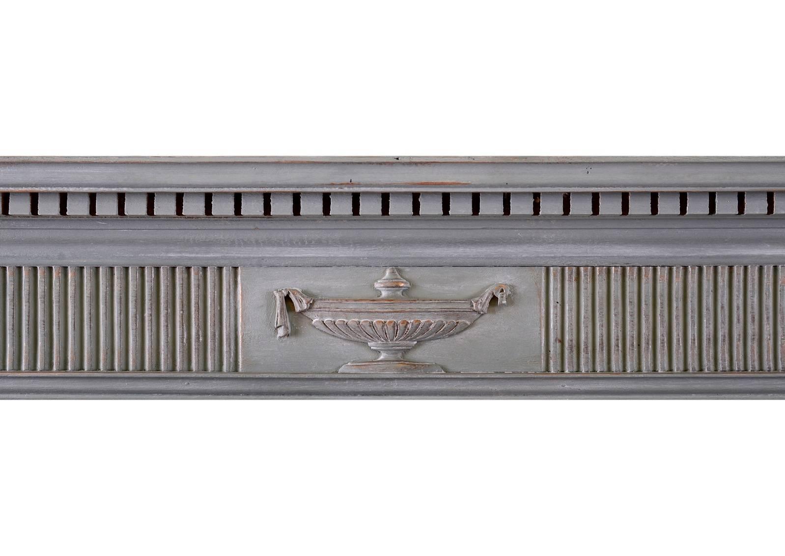 A small and delicate wood fireplace in the Regency style. The jambs surmounted by fluted frieze with carved classical urn to centre. Moulded shelf above. English. Currently painted light blue with elements of gold leaf effect behind. Could be