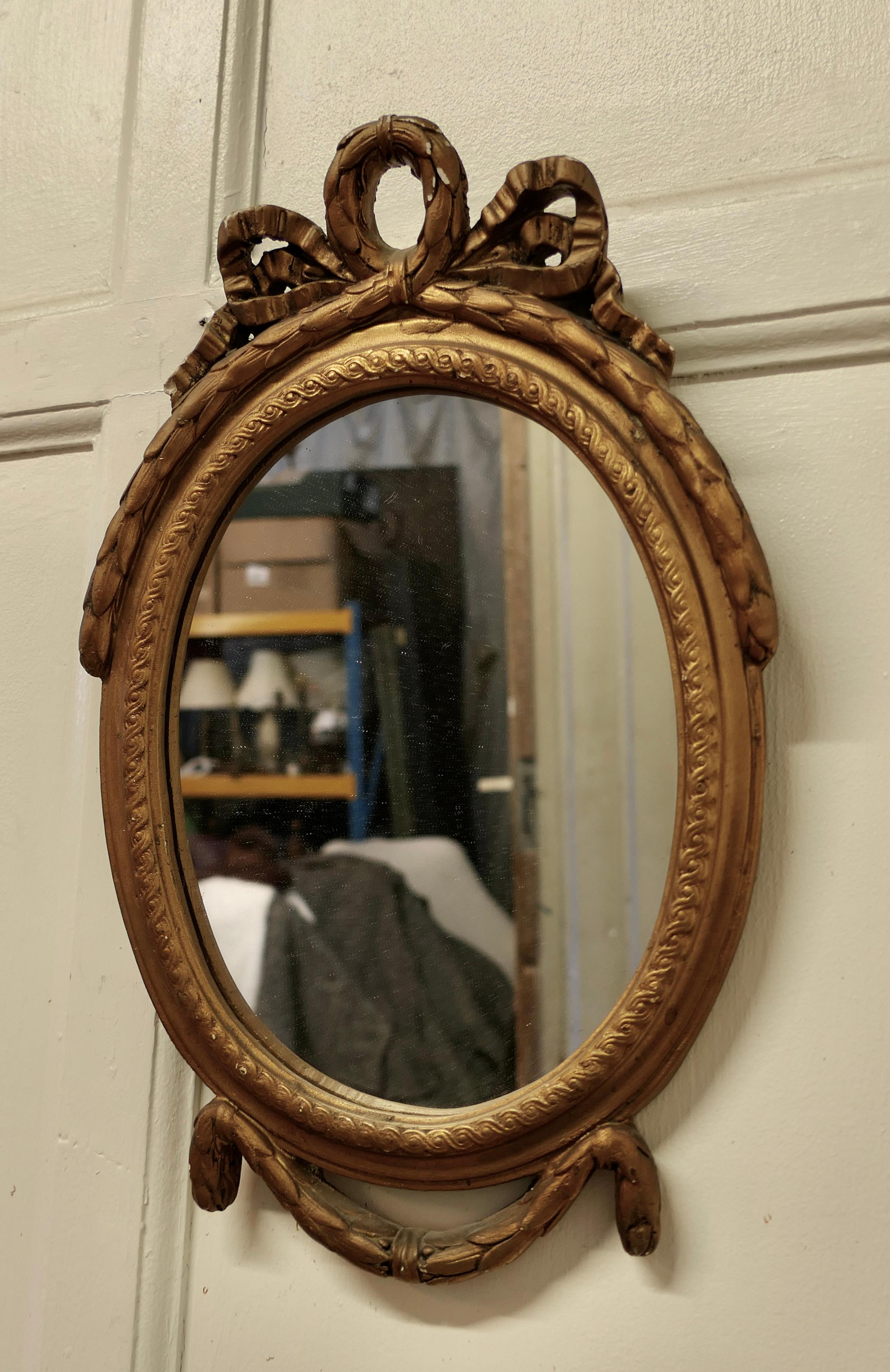 Small Rococo Oval Gilt Wall Mirror 

The Mirror has an exquisite age darkened gilt Frame in the Rococo Style, it has a oval  shape and decorated with ribbons at the top and a swag  design at the bottom 
The mirror is 12” wide and 19” tall and 2”