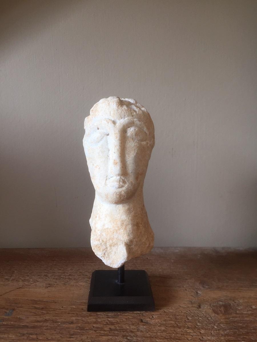 A small Romanesque marble head. Sculpted in a typical early medieval style it has an abstract approach to the human face. This reminds us of earlier representations as South east Arabian steles and even more modern artists as Brancusi. As art