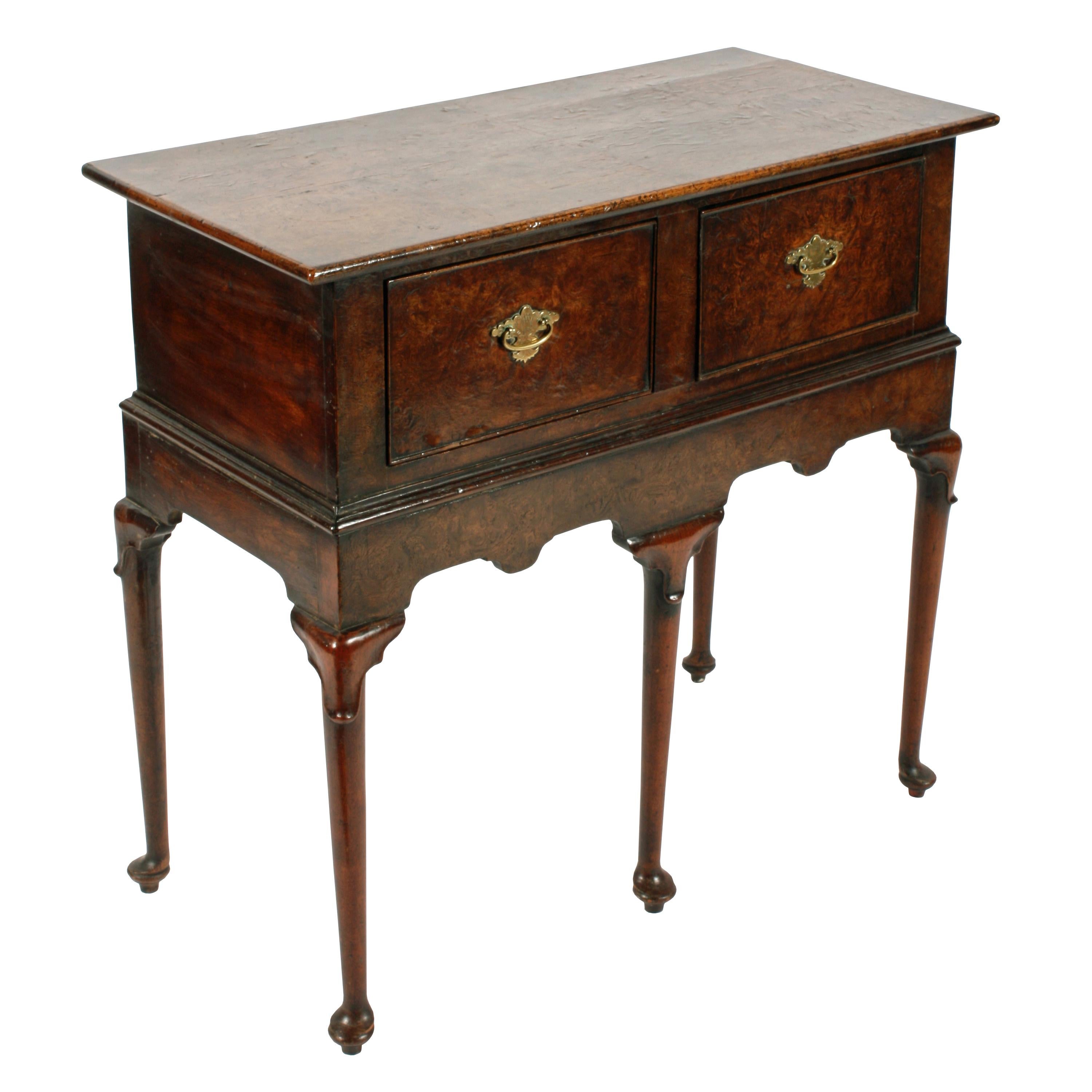 An early 18th century style small two drawer dresser base.

The dresser base stands on five turned legs that have pad feet and lappet carved knees.

The top, drawer fronts and surrounding frieze are burr elm, the legs, sides and mouldings are