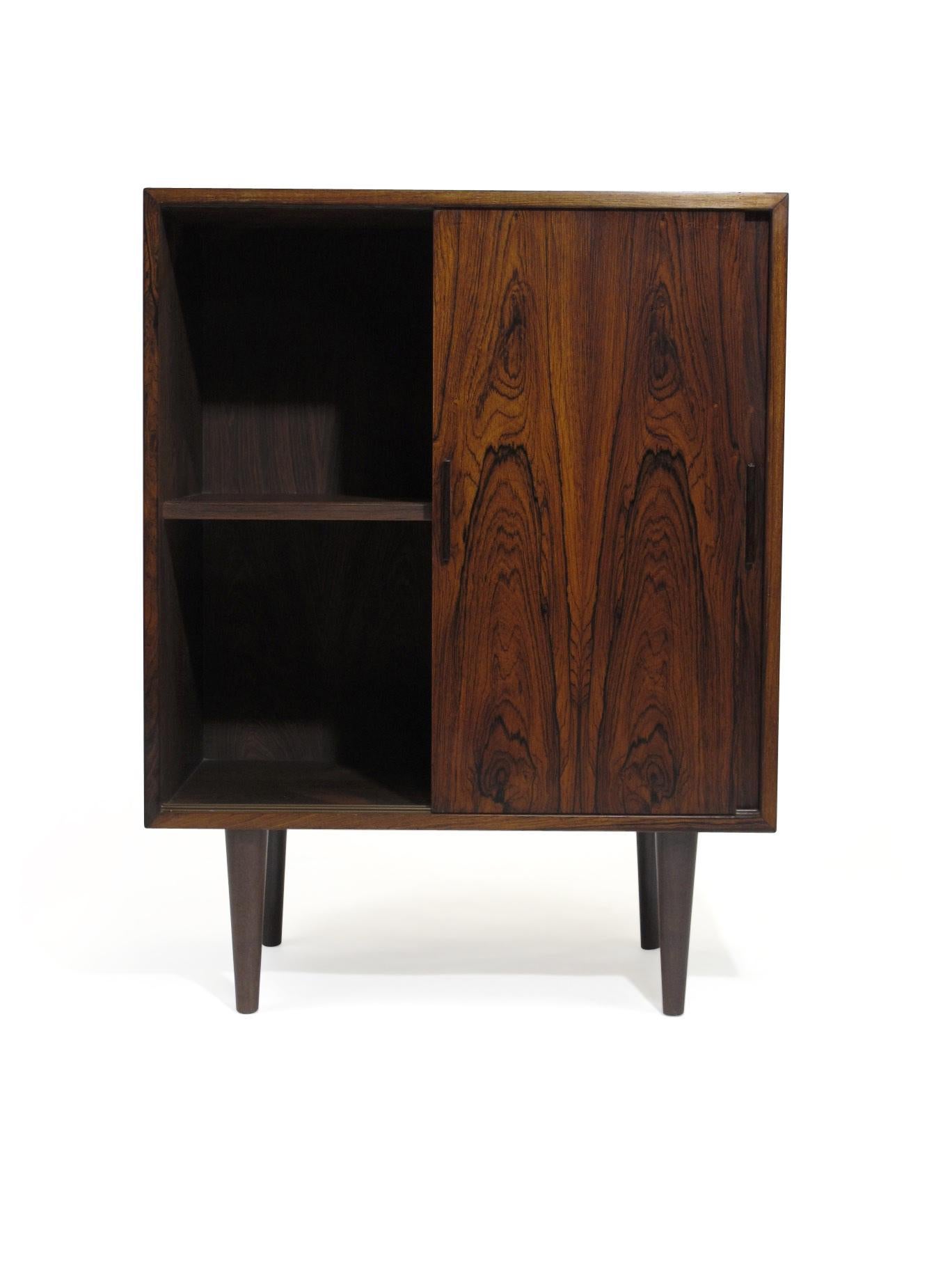 Mid Century Danish Modern Rosewood cabinet of dark book-matched rosewood with mitered edges, two sliding doors with interior lined with rosewood and interior shelf, raised on tapered legs. Cabinet can be use as entry way cabinet, media cabinet or