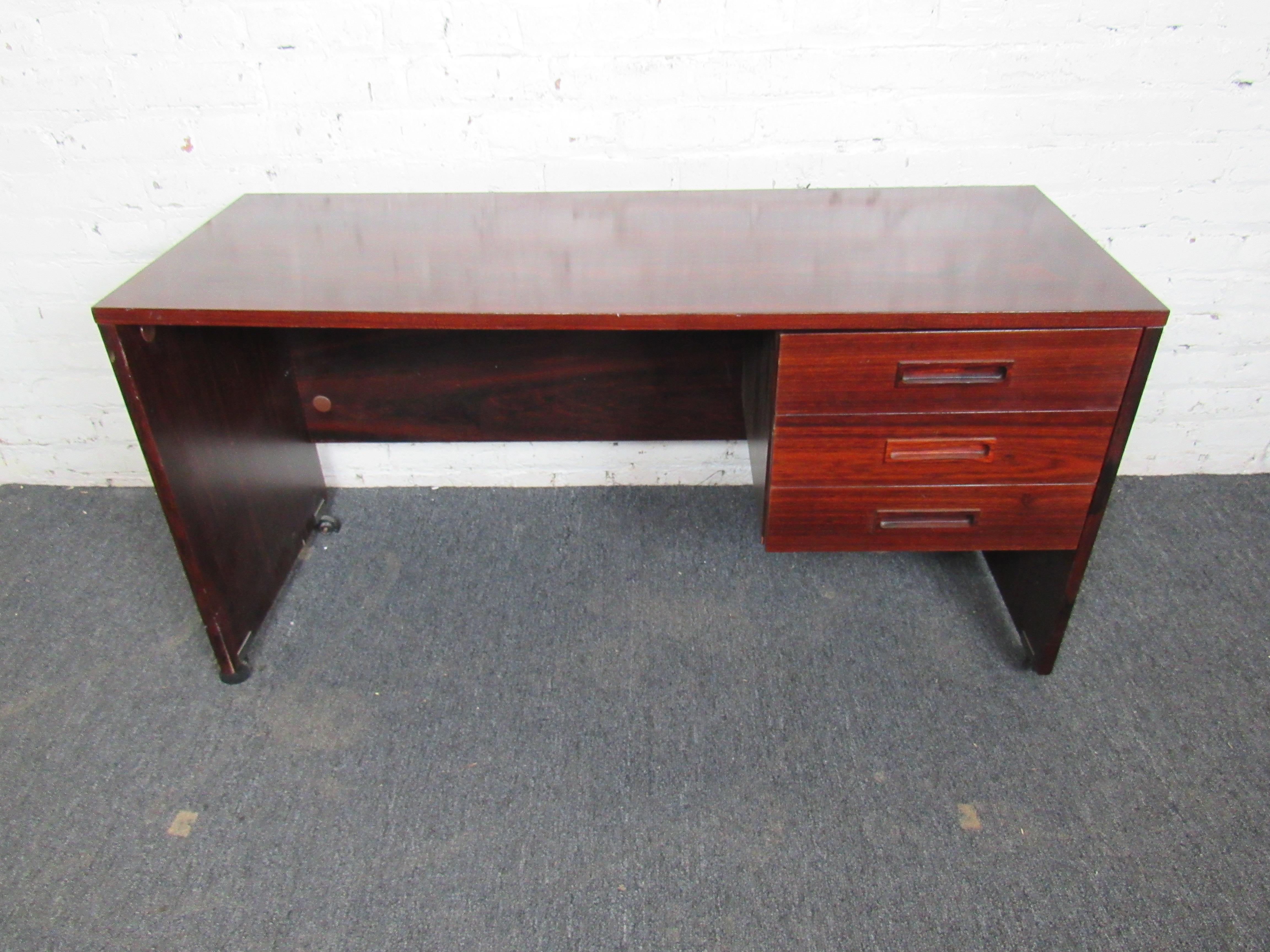 Vintage writing desk on rolling wheels, in an incredible rich rosewood color. This compact desk is functional and stylish, with a minimal design and three drawers for organization. Please confirm item location with seller (NY/NJ).