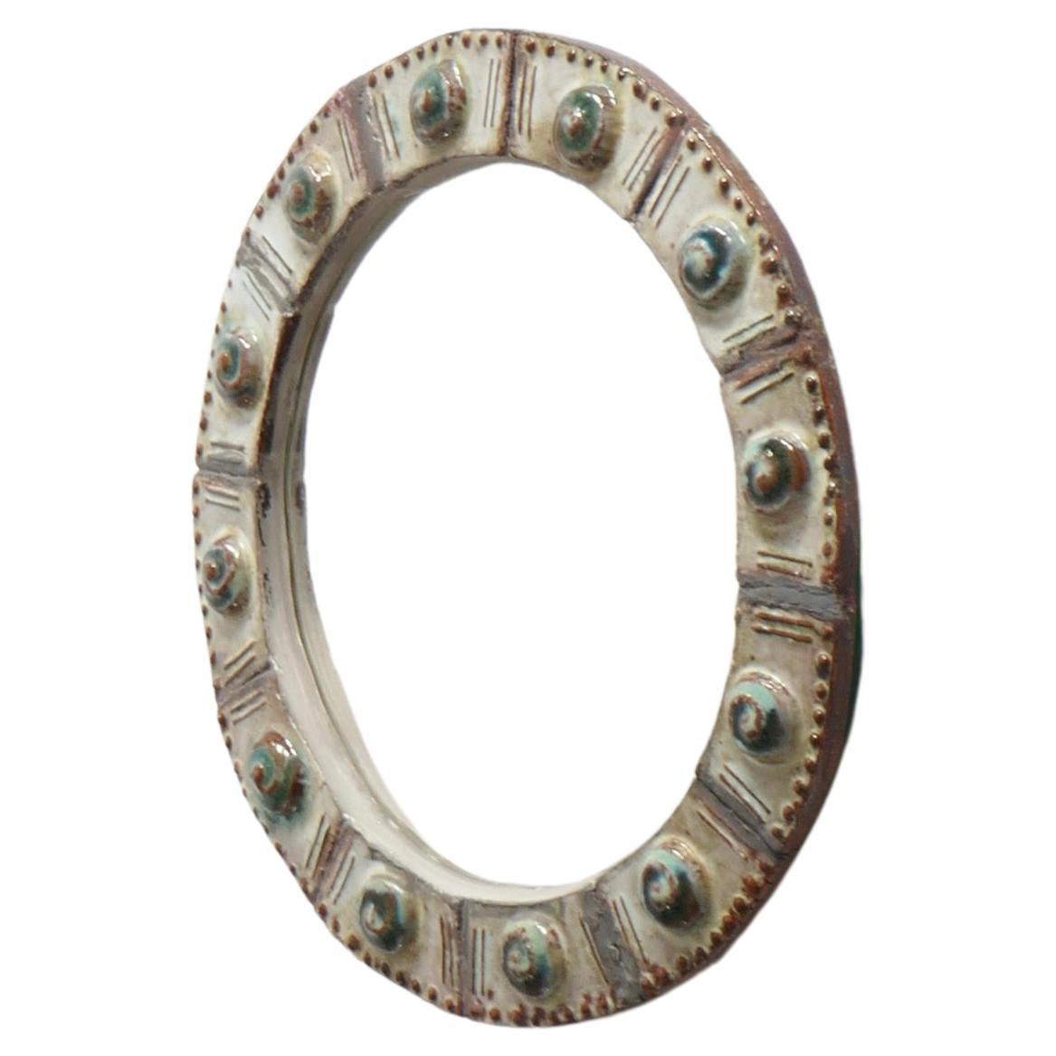 Small round ceramic mirror in white tones embellished with raised round patterns in a shade of green and ocher or terracotta. French work from the 1960s. It does not have a hook on the back but you can attach an invisible plate hanger for wall