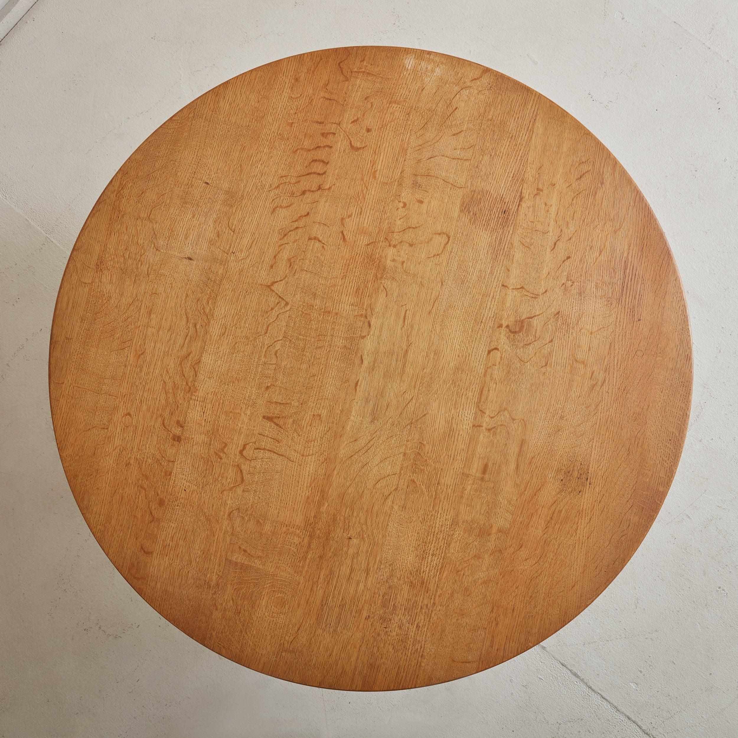 A charming round coffee table constructed of natural grained solid oak in a warm, honey hue. The Mid Century-Modern, Baroque-inspired silhouette features a scalloped apron, four sculpted legs, and a stretcher base with carved details. Attributed to