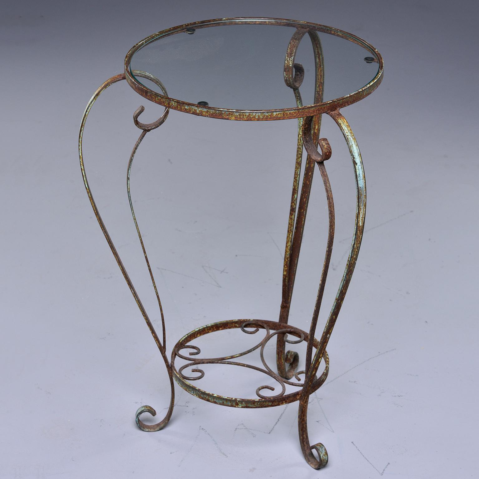 Found in France, this circa 1930s side table has a curvy iron frame with a green painted finish and clear, round glass top. This table can be used indoors or out. Unknown maker.