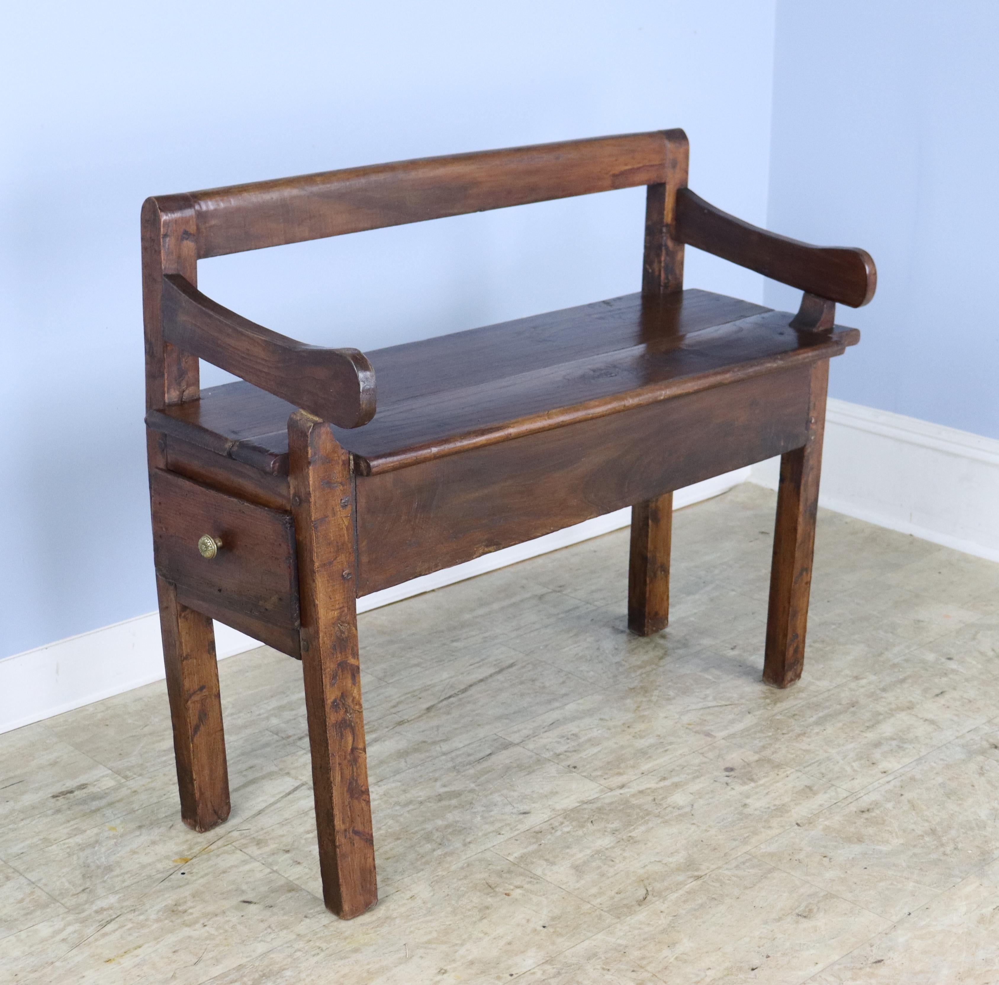 A small handmade French bench in glossy chestnut with a long drawer in the seat.  The irregular planks and quirky silhouette add charm, and have no effect on the stability of the piece.  No wobbling!  Good chestnut color and patina.  Quite