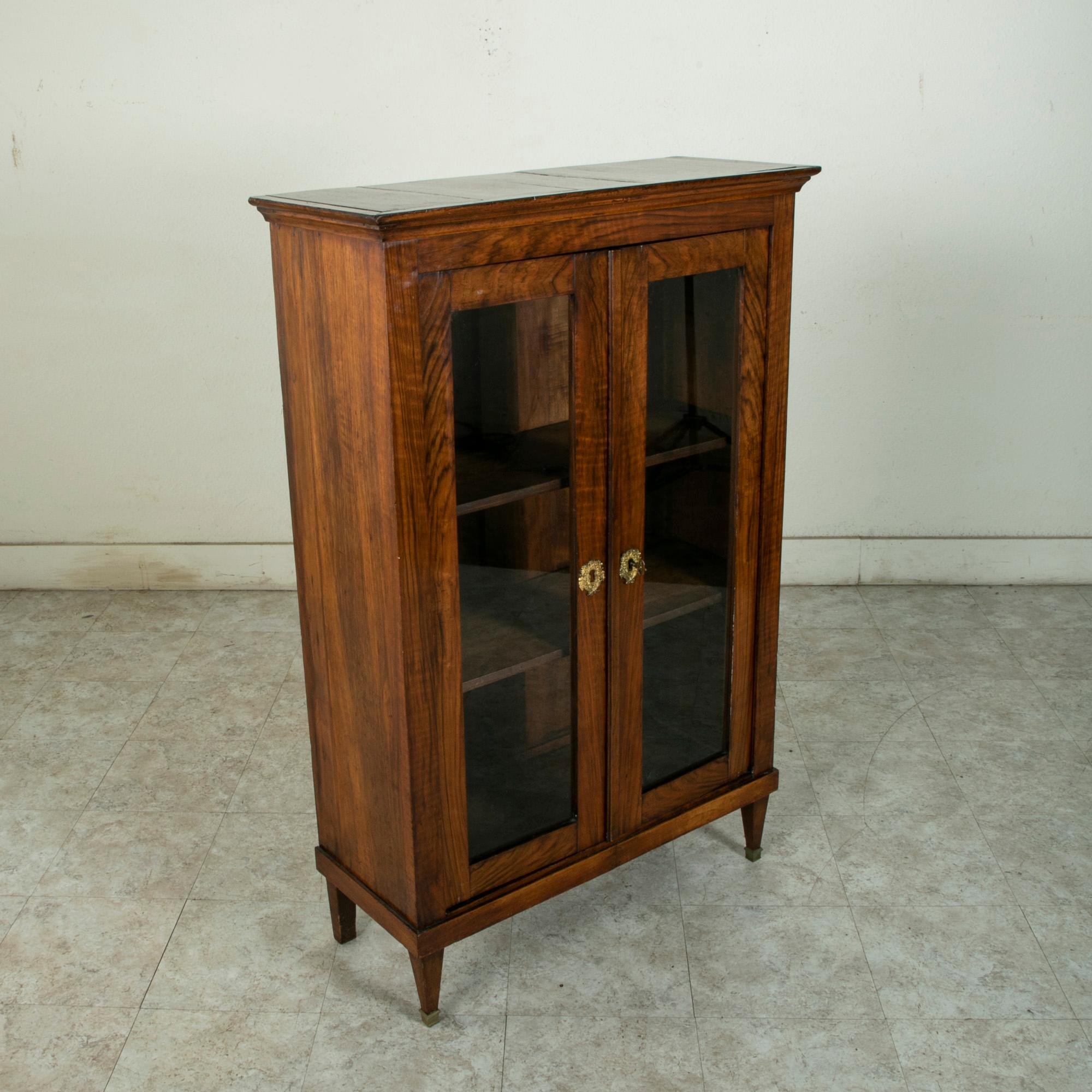 Standing at 51 inches in height, this small scale late eighteenth century French Louis XVI period palisander bookcase or vitrine features its original hand blown glass doors. The doors are appointed with bronze escutcheons detailed with cornucopia