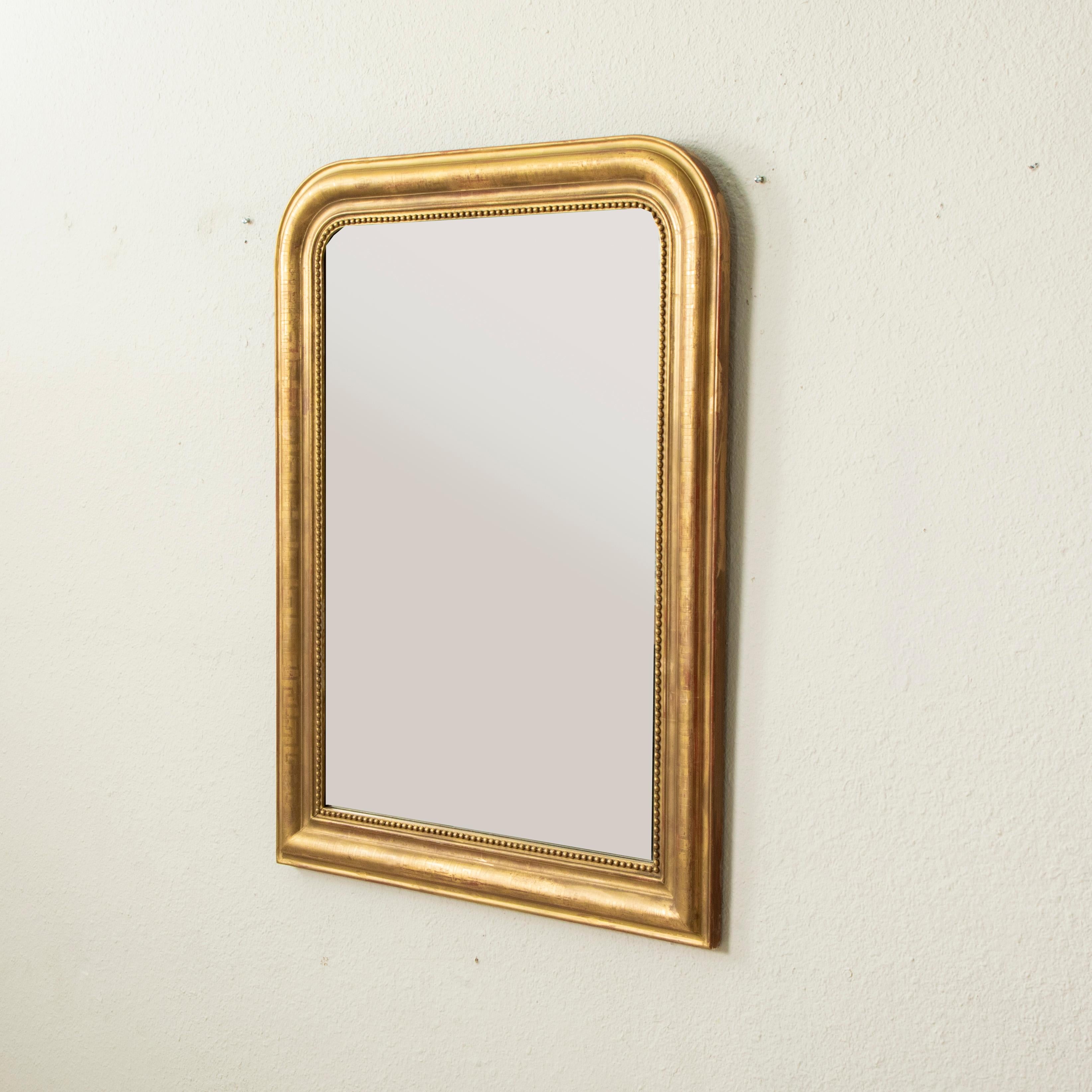 This small-scale nineteenth century Louis Philippe period gilt wood mirror features a pillow frame detailed with a subtle incised Greek key motif and an inner border of fine beading. Its original iron oxide under-body gives it a rich glow, and the