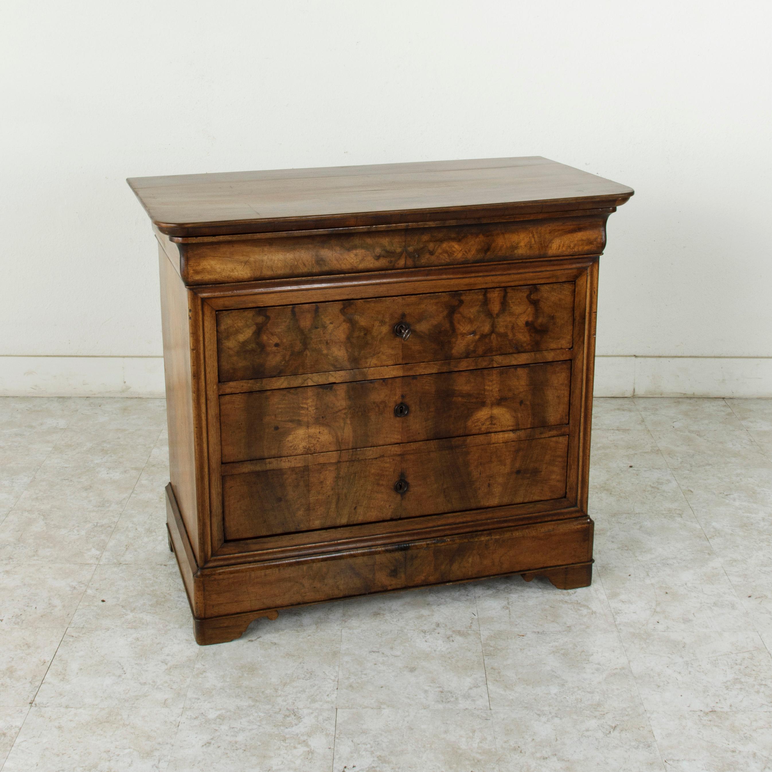 Rare for its smaller scale with a 41 inch width, this quintessential Louis Philippe period commode or chest of drawers displays the exemplary craftsmanship of the early 19th century with a facade of book matched walnut and solid walnut panel sides