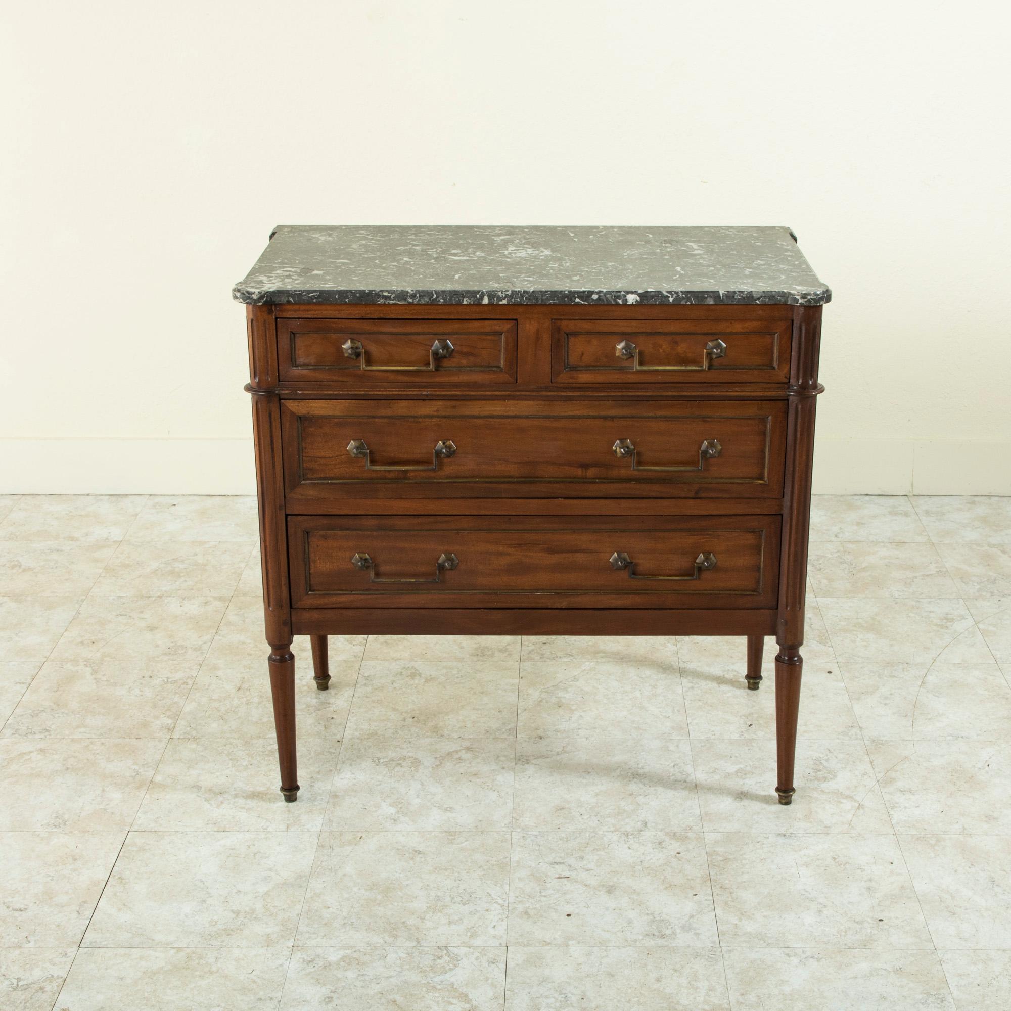 Measuring only 35 inches wide, this small scale mid-nineteenth century French Louis XVI mahogany commode or chest of drawers features a beveled Saint Anne marble top and fluted rounded corners. Its four drawers of dovetail construction are detailed