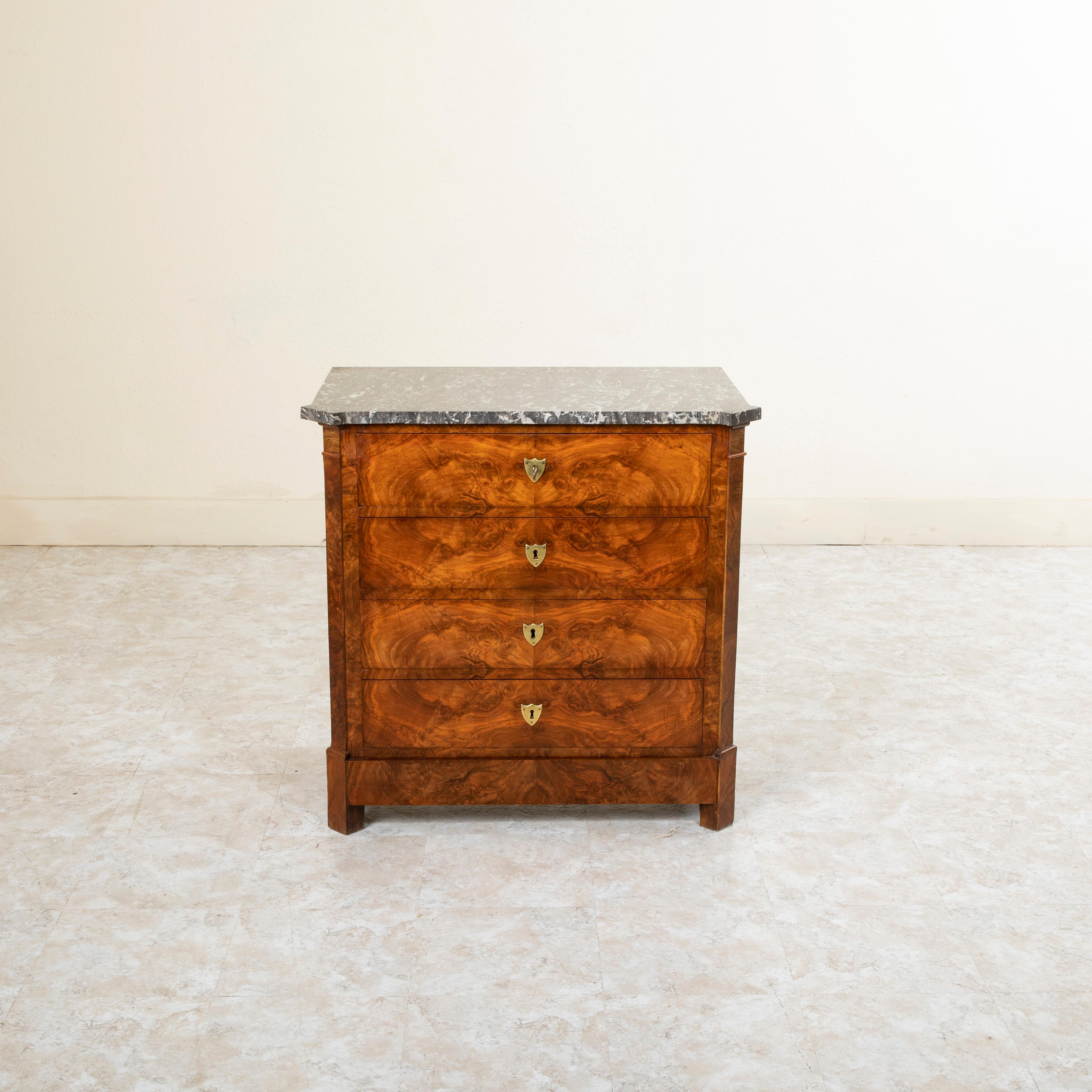 With only a 32.25 inch width, this small scale early nineteenth century French Restauration period commode or chest of drawers displays exemplary craftsmanship with a facade of book matched burl walnut, solid walnut panel sides, and a Saint Anne