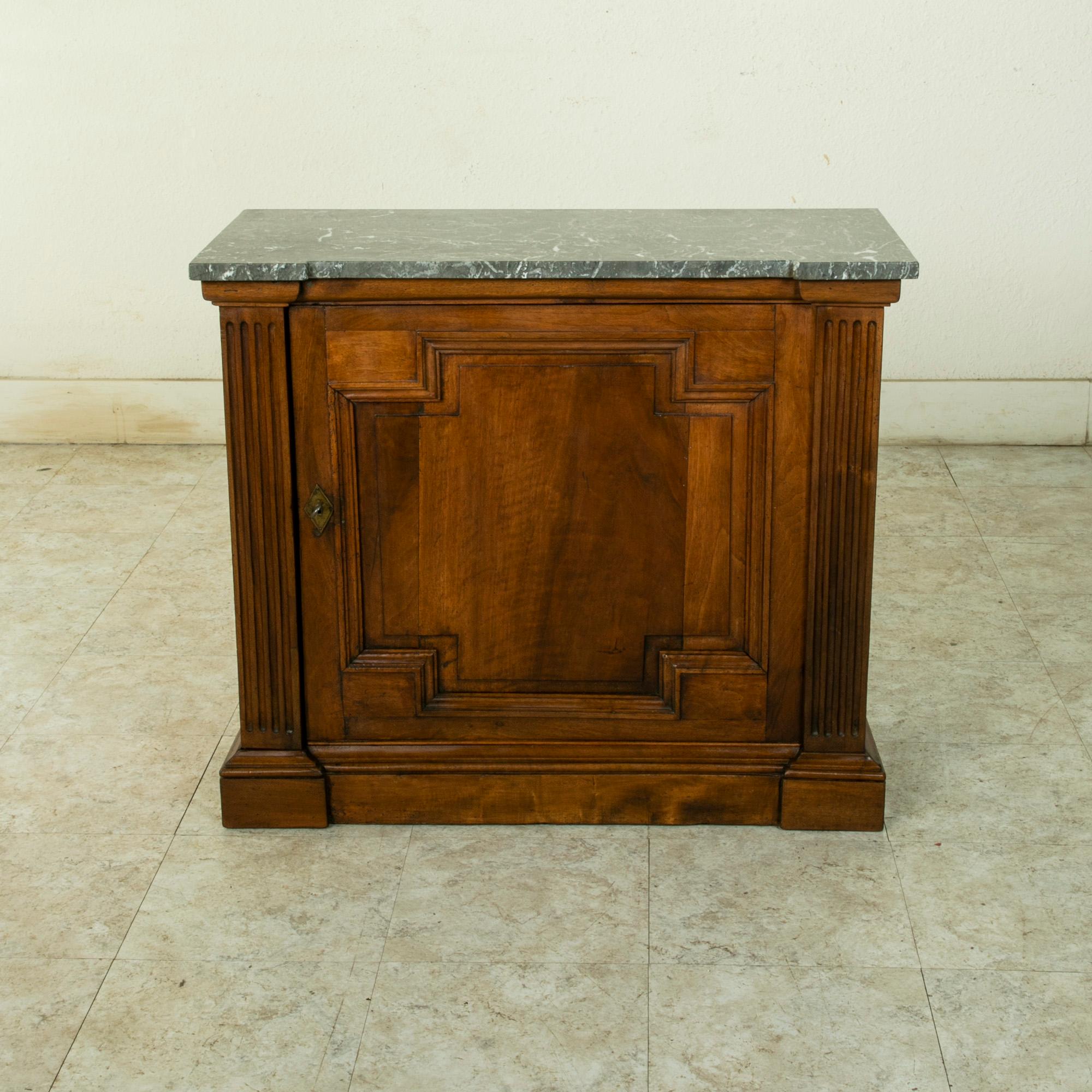 This small scale late 19th century French walnut cabinet features a Saint Anne marble top. Fluted columns at the corners flank the door. The paneled door is framed with indented corners and opens to reveal an interior with a single adjustable shelf.