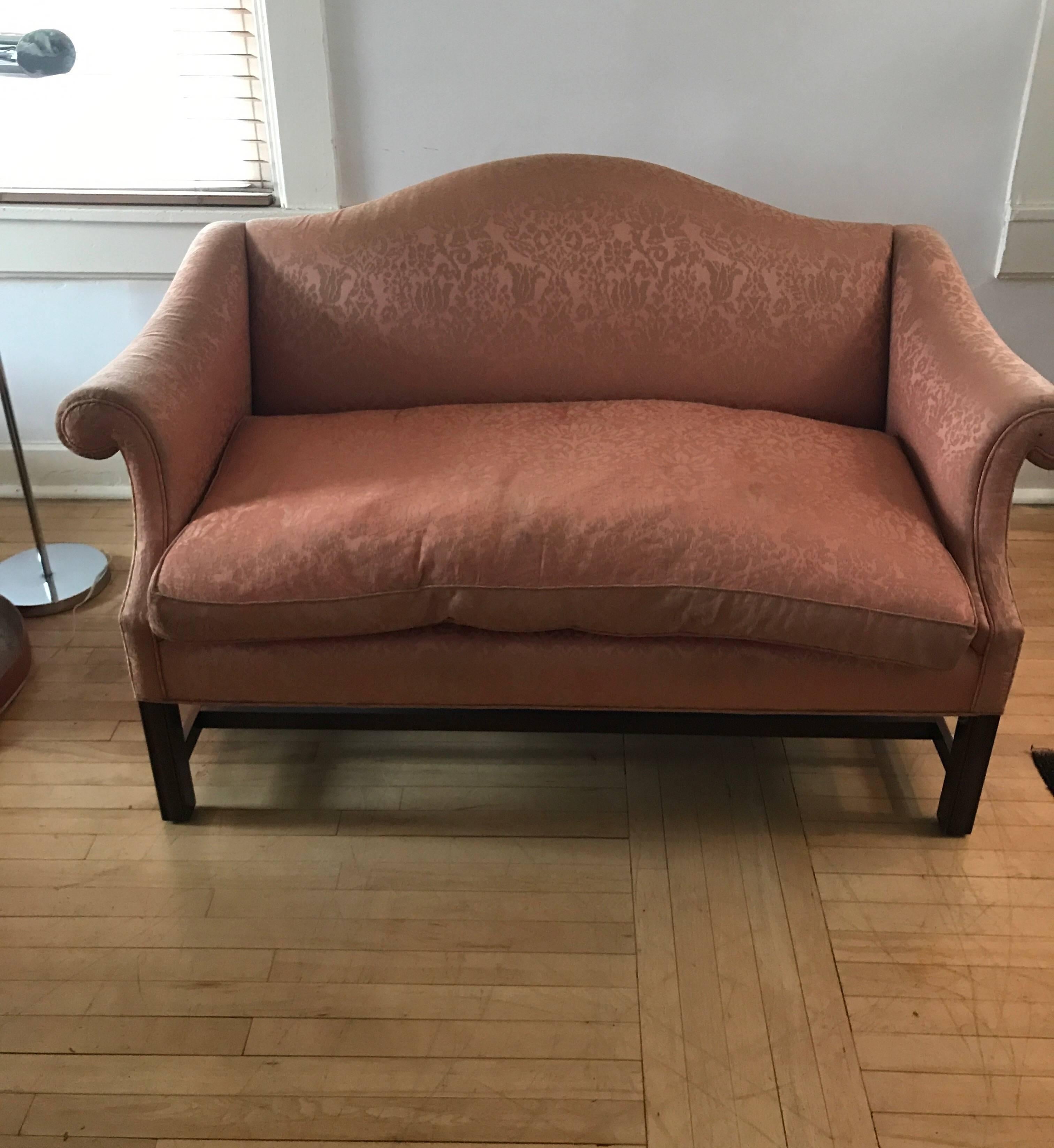 An elegant small scale Chippendale style mahogany camelback sofa loveseat.
The sofa has a classic arched back with gently rolled arms. The loveseat is upholstered in damask 
and has a single down filled cushion. The front legs are square Marlboro