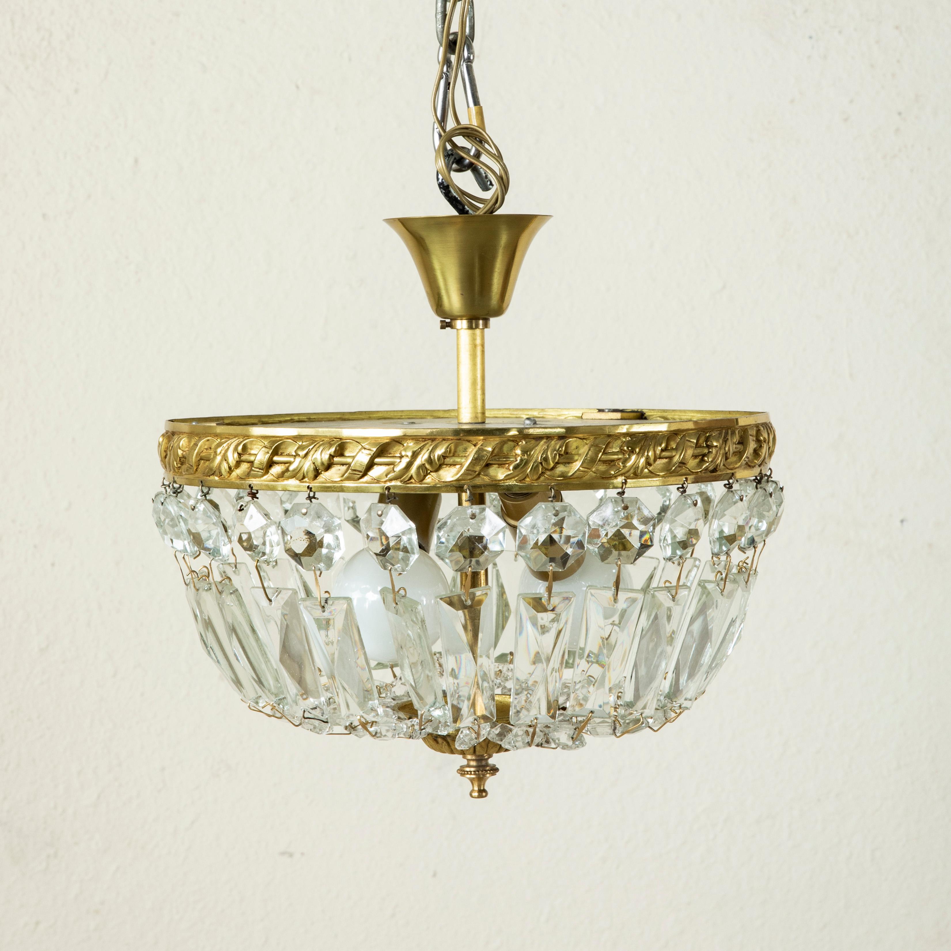 This small scale early 20th century French flush mount chandelier features an upper bronze ring with a scrolling leaf motif. Multi-faceted strings of crystal beading drape to meet a lower finial detailed with palmettes. An ideal chandelier for a