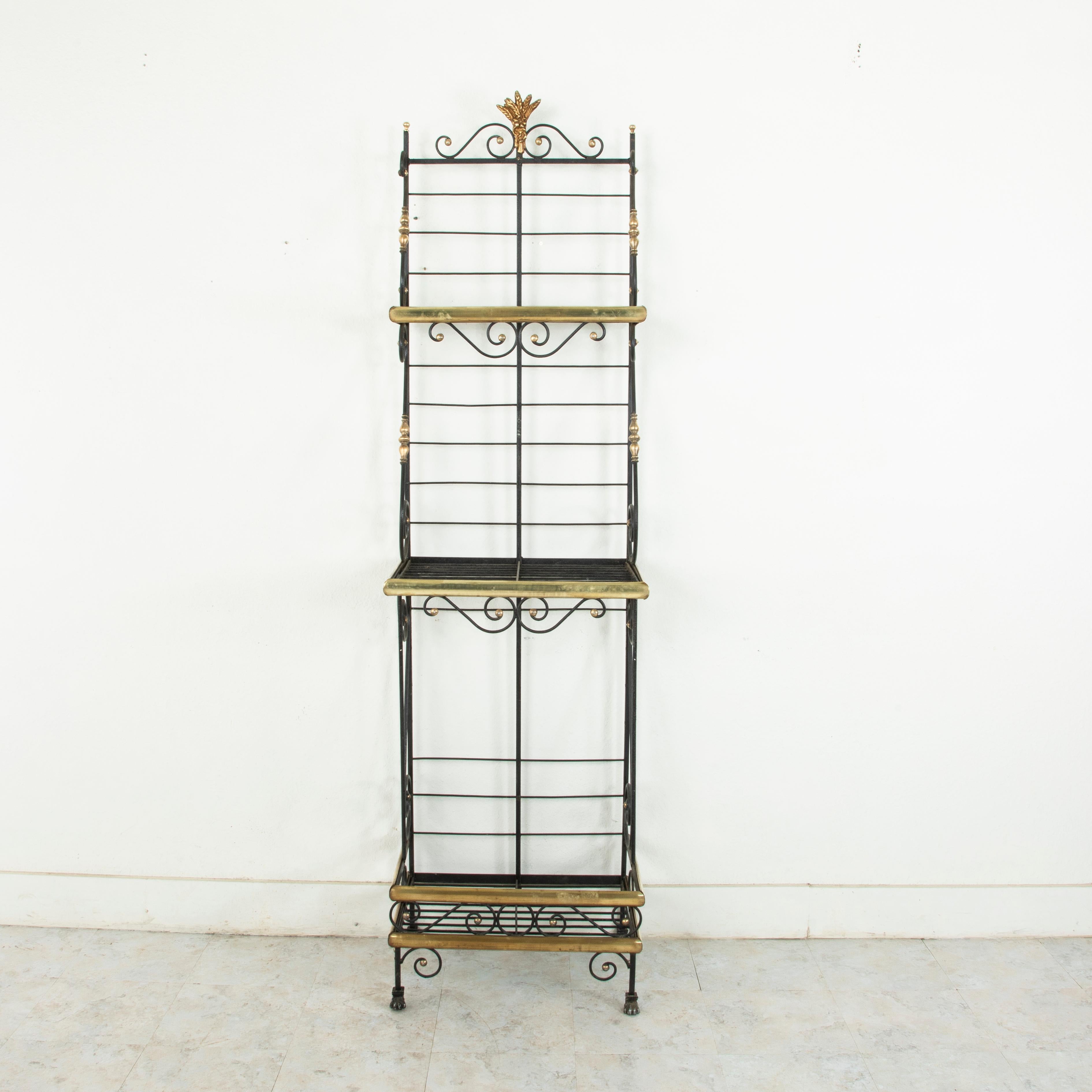A rare find in a unique small scale, this mid-20th century French iron baker's rack is trimmed in brass around each of its three shelves. The shelves are joined by scrolling iron detailed with brass turnings that lend support as well as an aesthetic