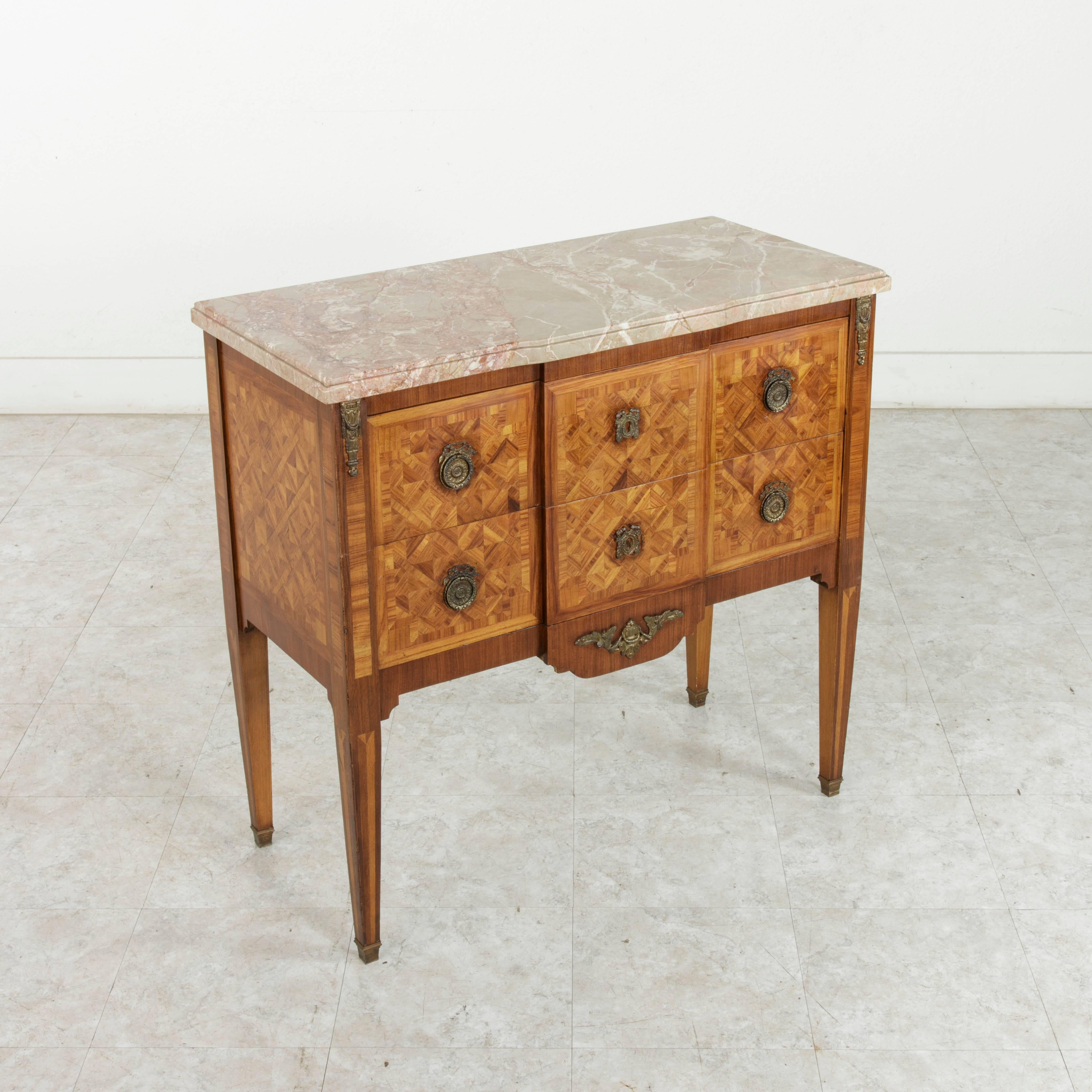 This small-scale early 20th century Louis XVI style commode or chest features geometric patterns of rosewood marquetry on three sides and is crowned with a bevelled marble top. Called a sauteuse in French, this fine chest has two drawers of dovetail