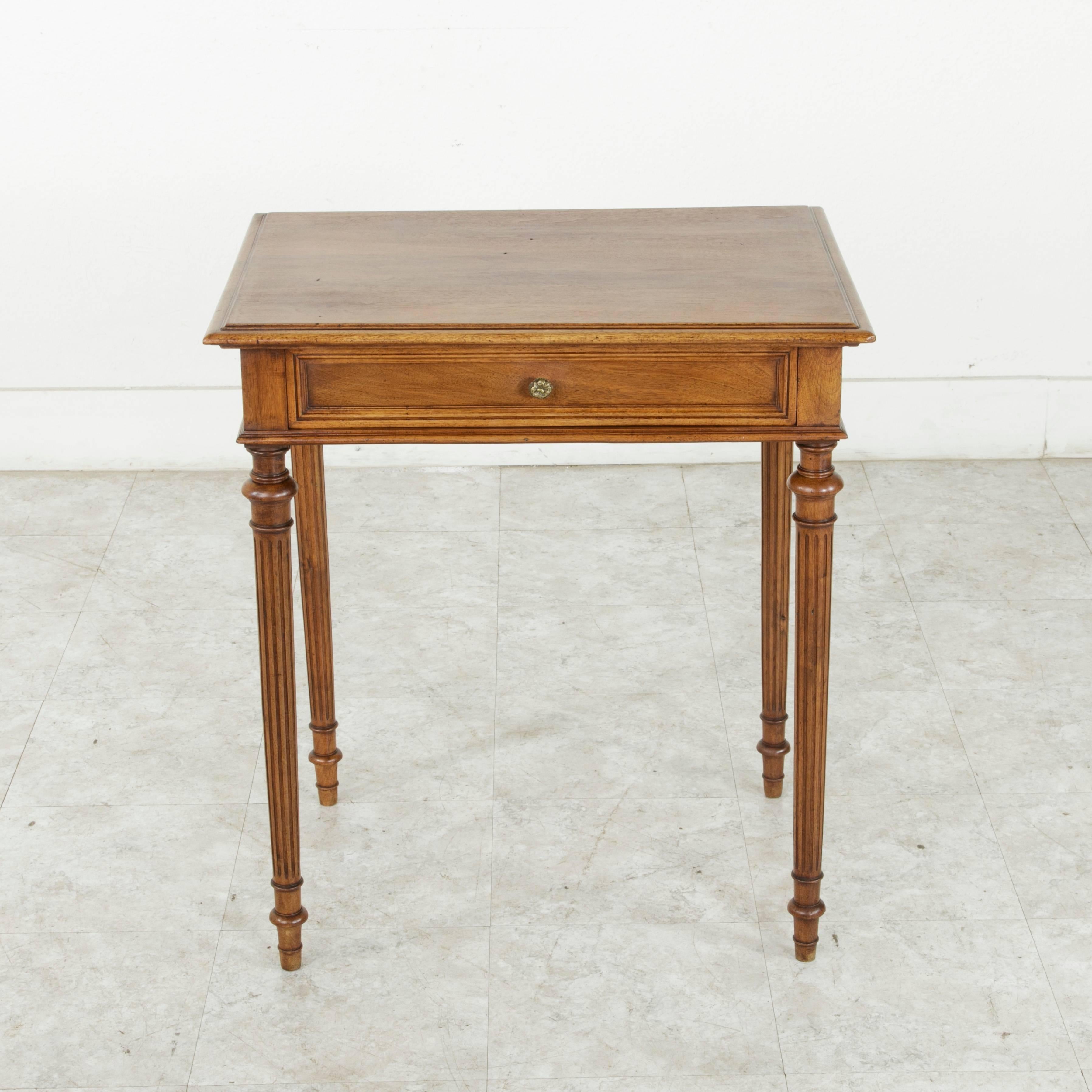 This small-scale French Louis XVI style walnut side table from the turn of the 20th century features classic tapered, fluted legs and a bevelled walnut top. A single drawer of dovetail construction with a bronze pull blends seamlessly with the