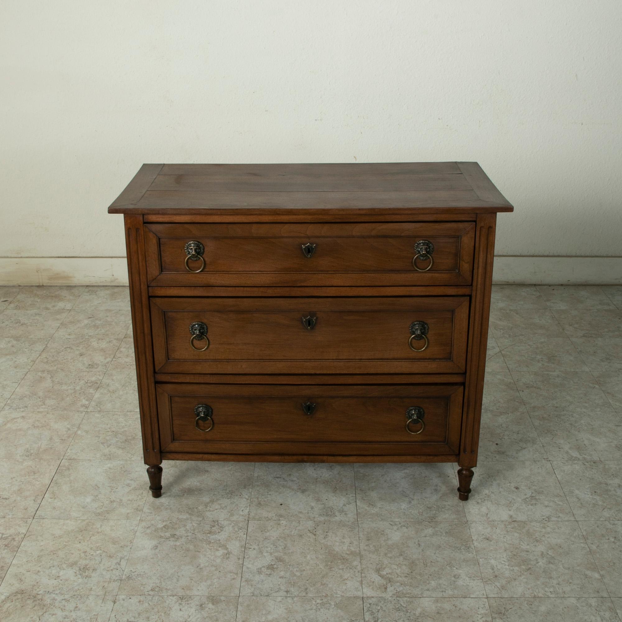 With a 40 inch width, this small scale late eighteenth century French Louis XVI period walnut commode or chest of drawers features a solid wood top, paneled sides, and fluted corners. Its three drawers of dovetail construction are appointed with