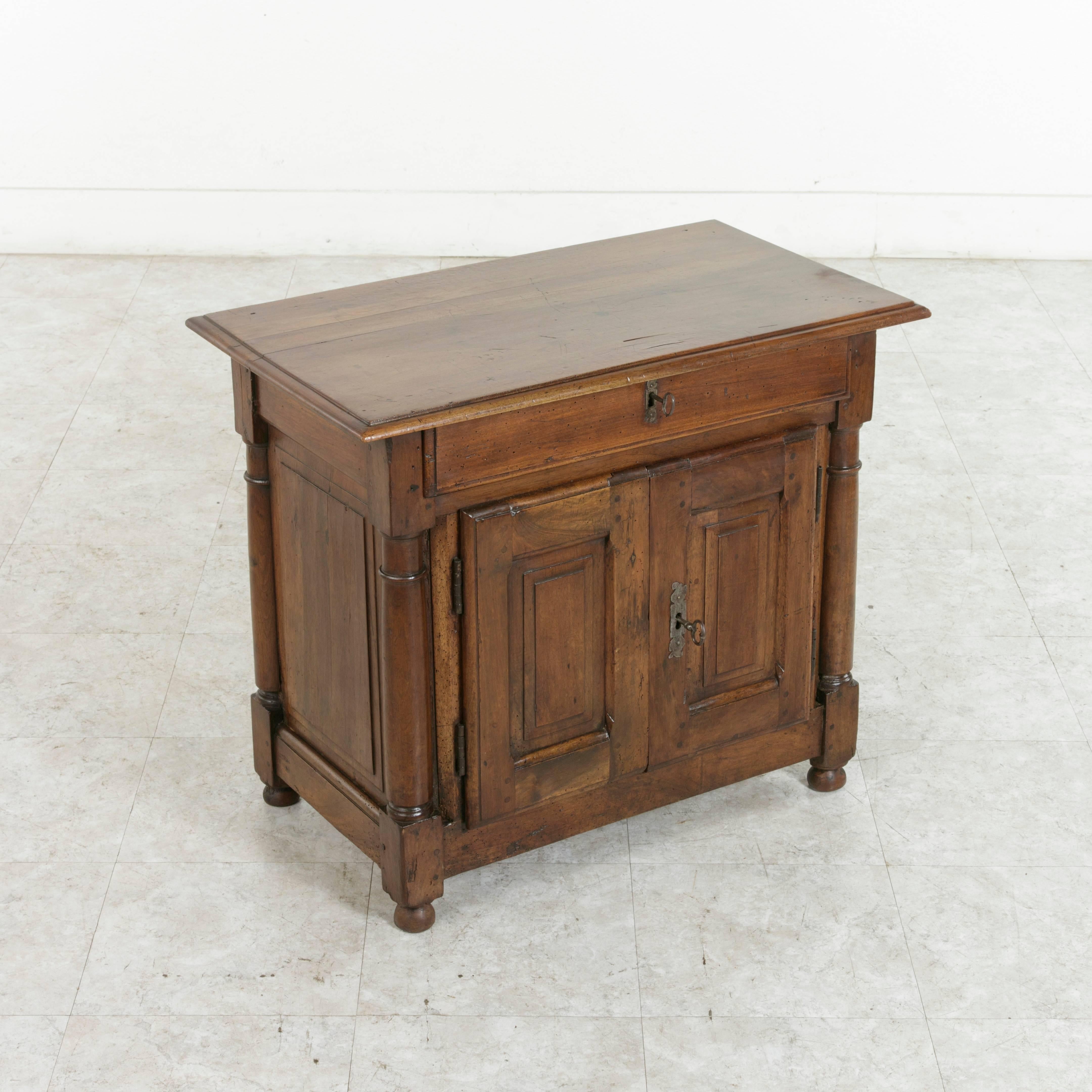 Originally used in a French convent, this small-scale late 18th century walnut cabinet or side table is uniquely double faced with raised panels on all sides and a hand-turned column at each corner. Hand pegged capitals and plinths and small bun